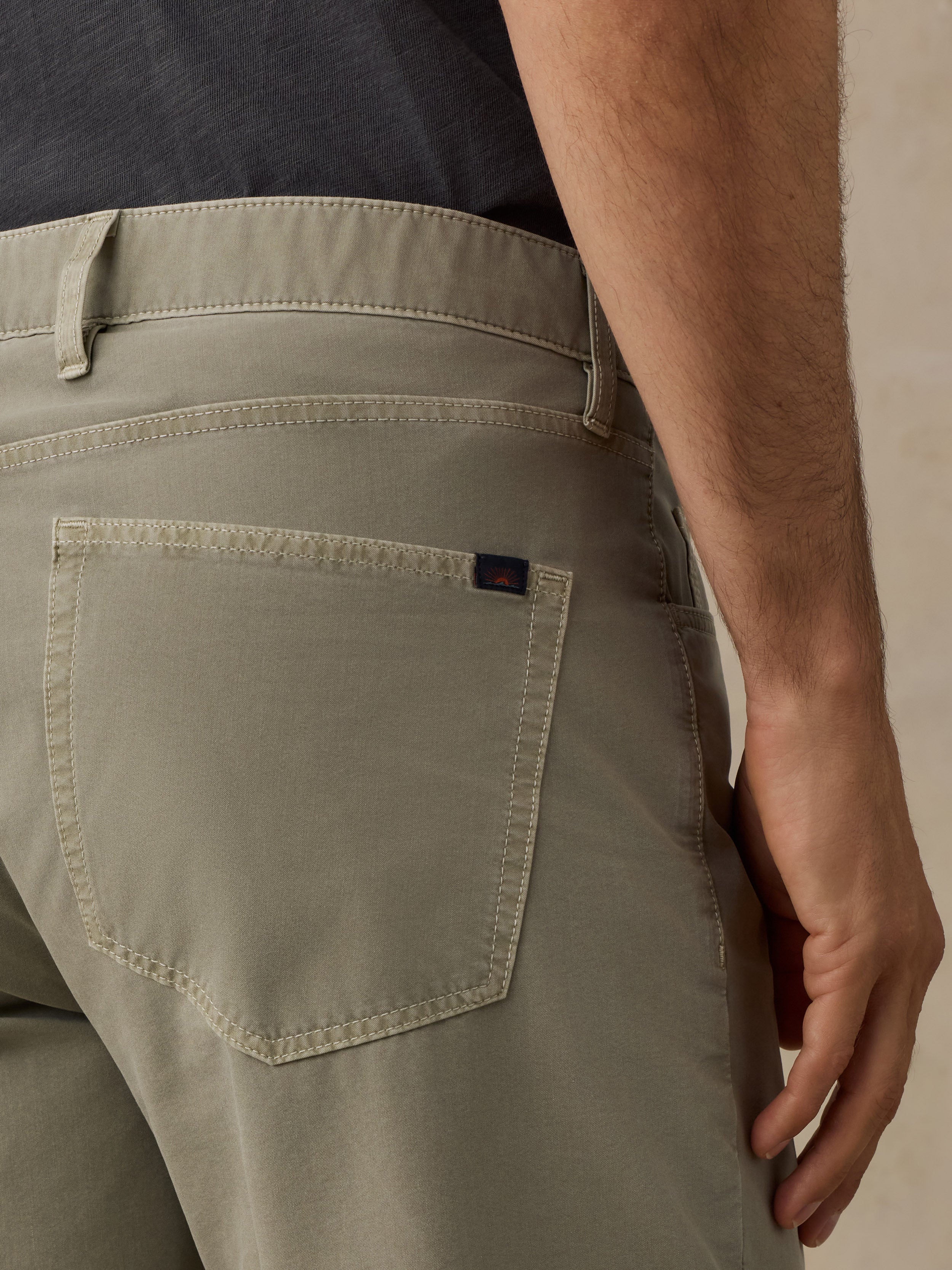 Close-up of a man wearing light khaki trousers, focusing on the back pocket with a small dark brand tab and waistband details.