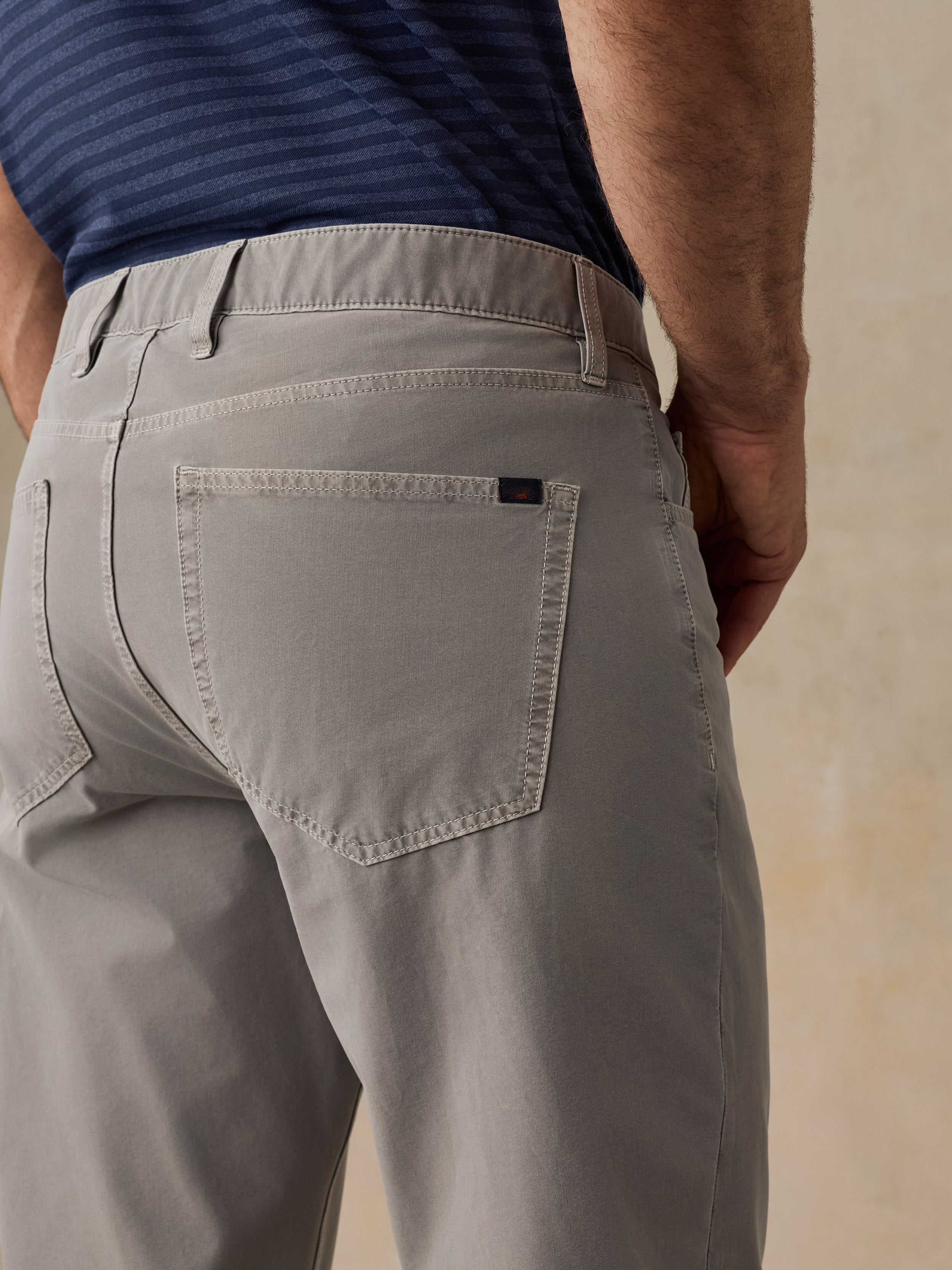 Close-up back view of a person wearing light gray trousers and a navy striped shirt, showing the back pocket and waistband details.