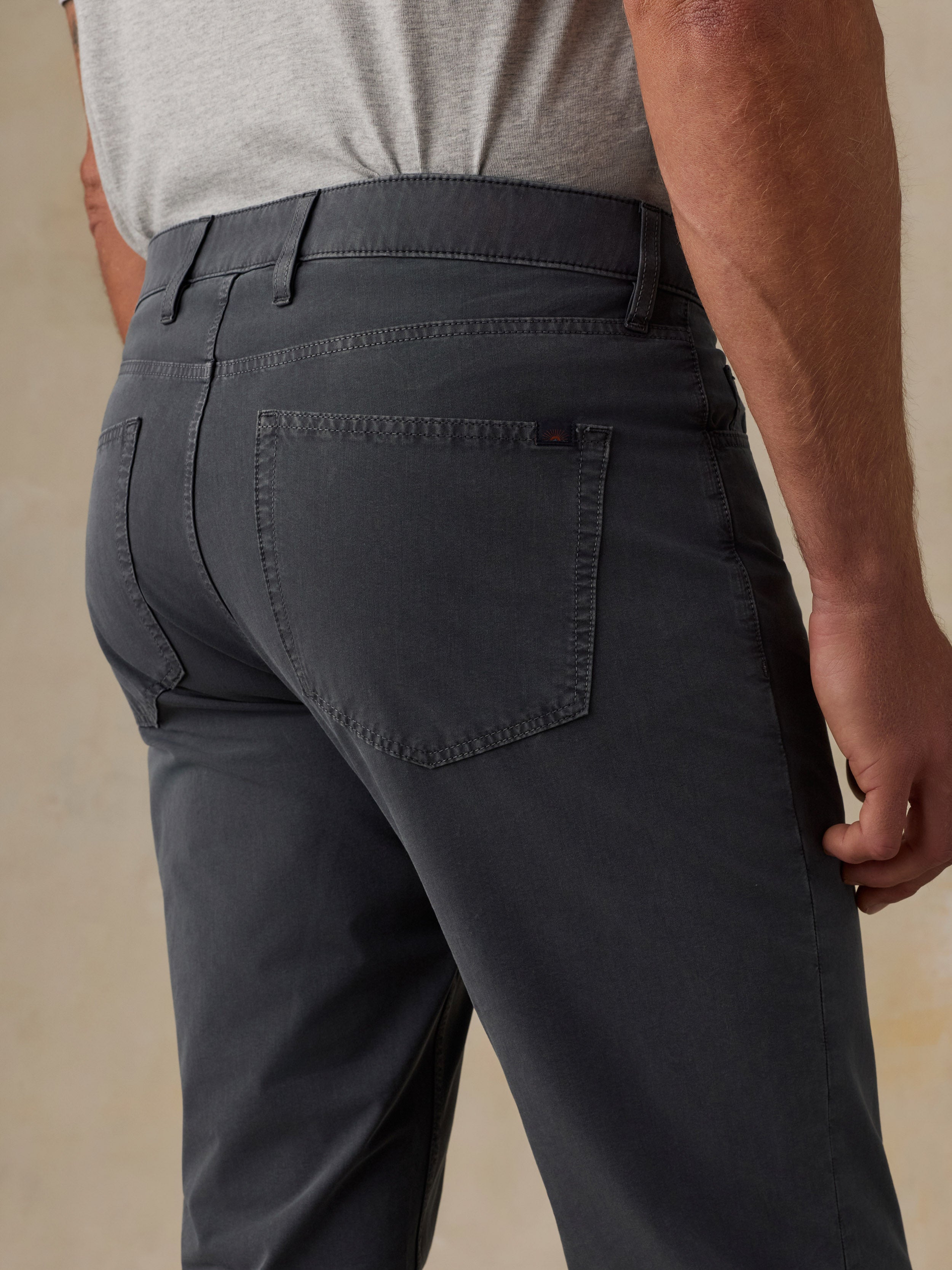 Close-up back view of a man wearing dark charcoal gray trousers with a light gray t-shirt, showing the back pocket and waistband details.