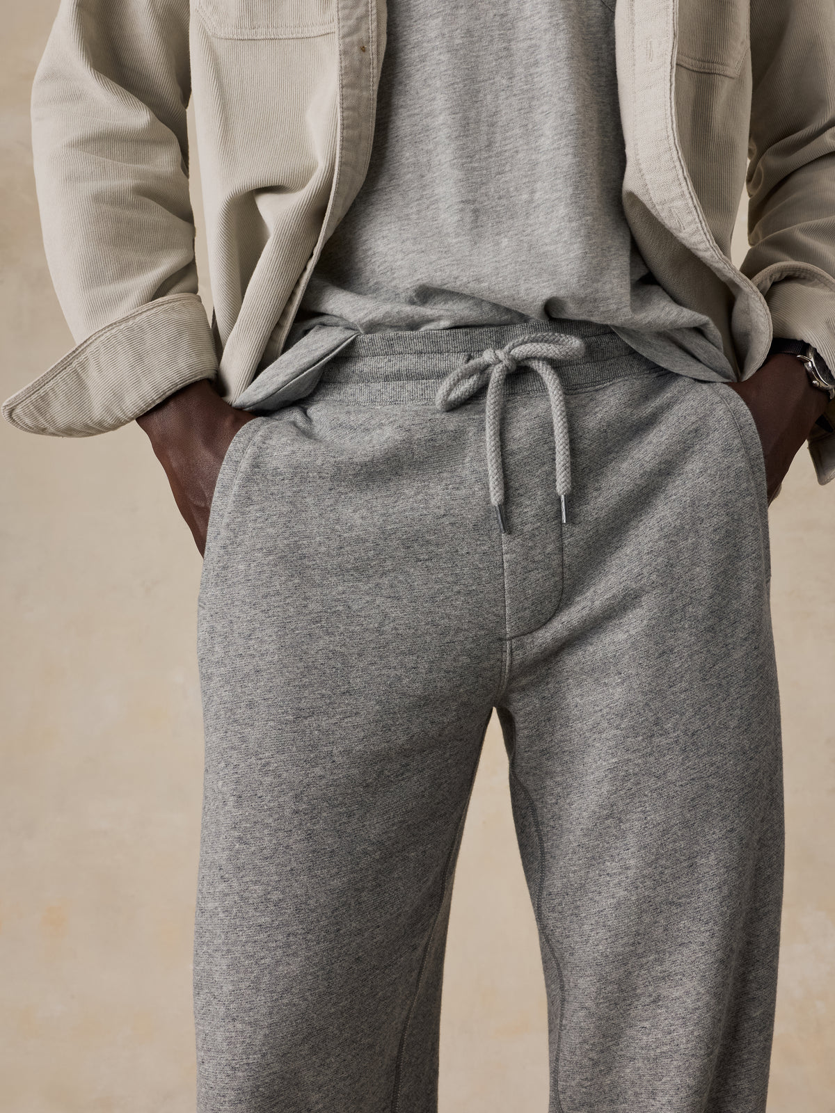 Close up of a man wearing grey sweatpants, grey t-shirt, and a beige overshirt, image 4 of 5
