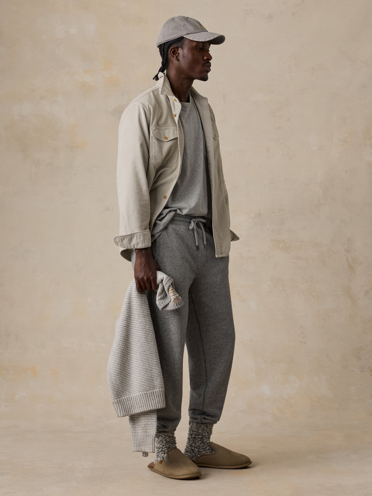 A man wearing grey sweatpants, a grey t-shirt, and a beige overshirt, image 5 of 5
