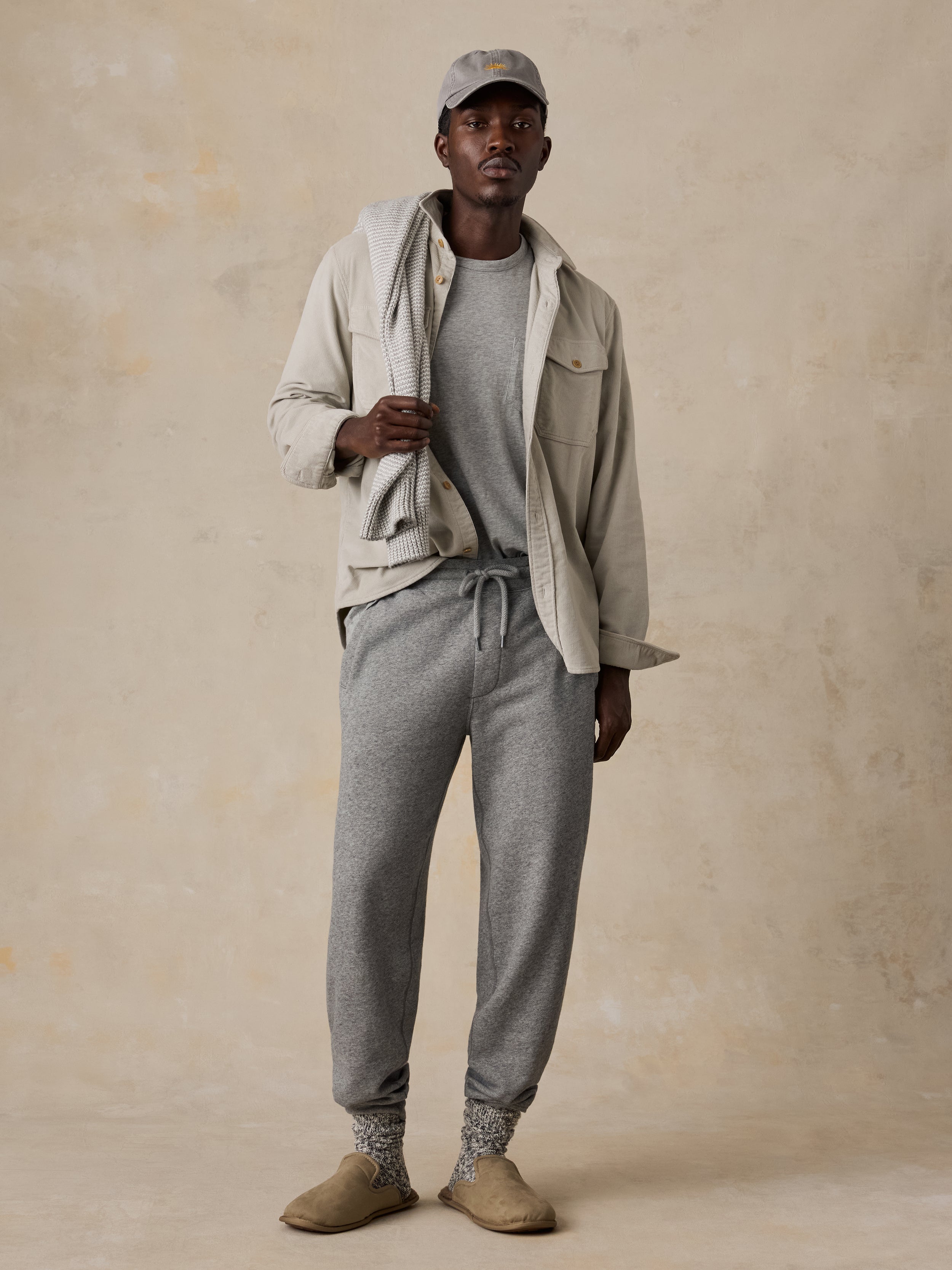 A man wearing grey sweatpants, a grey t-shirt, and a beige overshirt