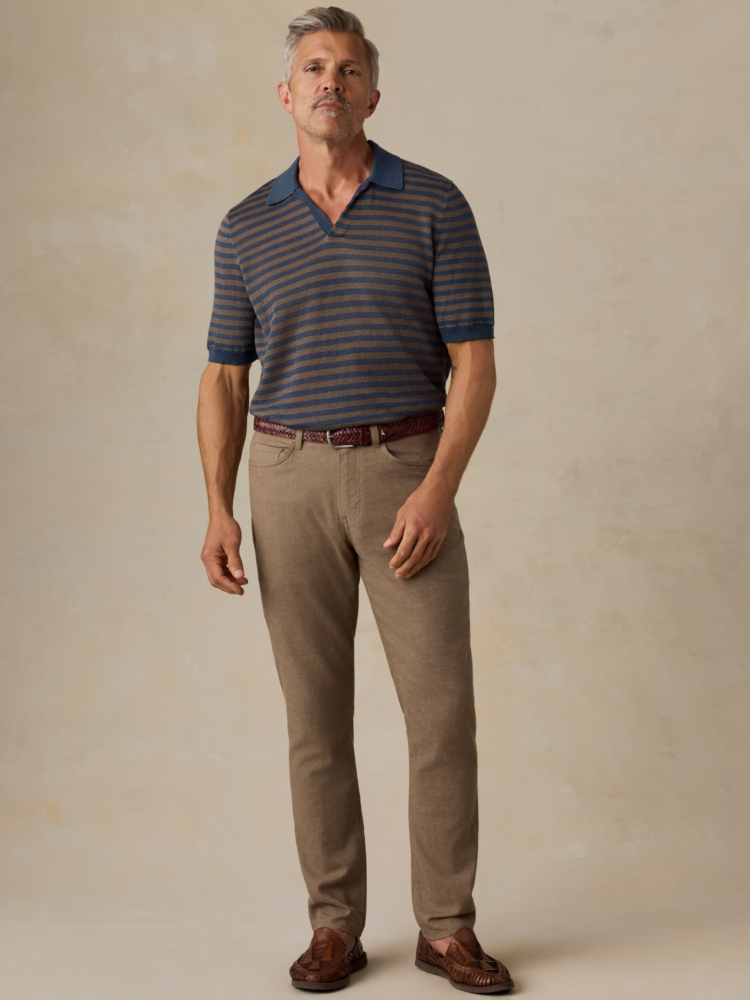 Man wearing green pants and a striped tee against a beige background