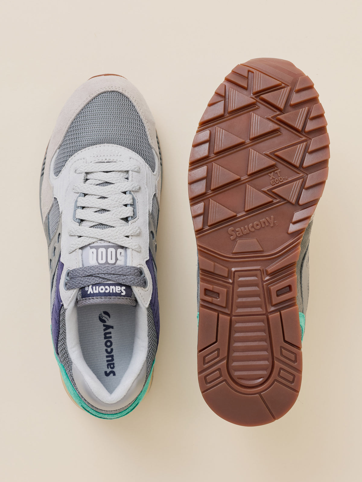A pair of Saucony sneakers shown from above on a light beige background, with one shoe displaying the side and the other showing the brown treaded outsole.