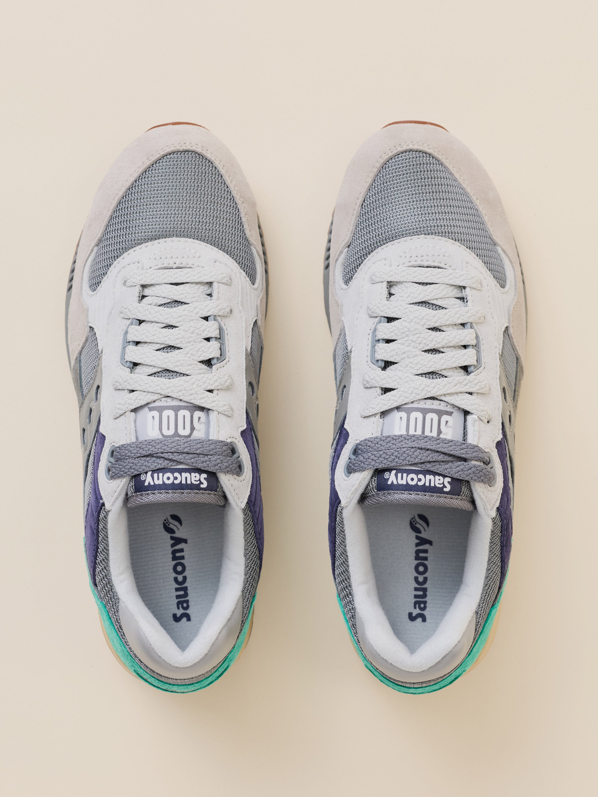 A pair of Saucony 500 sneakers shown from a top-down view on a light beige background. The shoes feature a white and gray mesh upper with gray overlays, white laces, and a small teal accent on the heel.