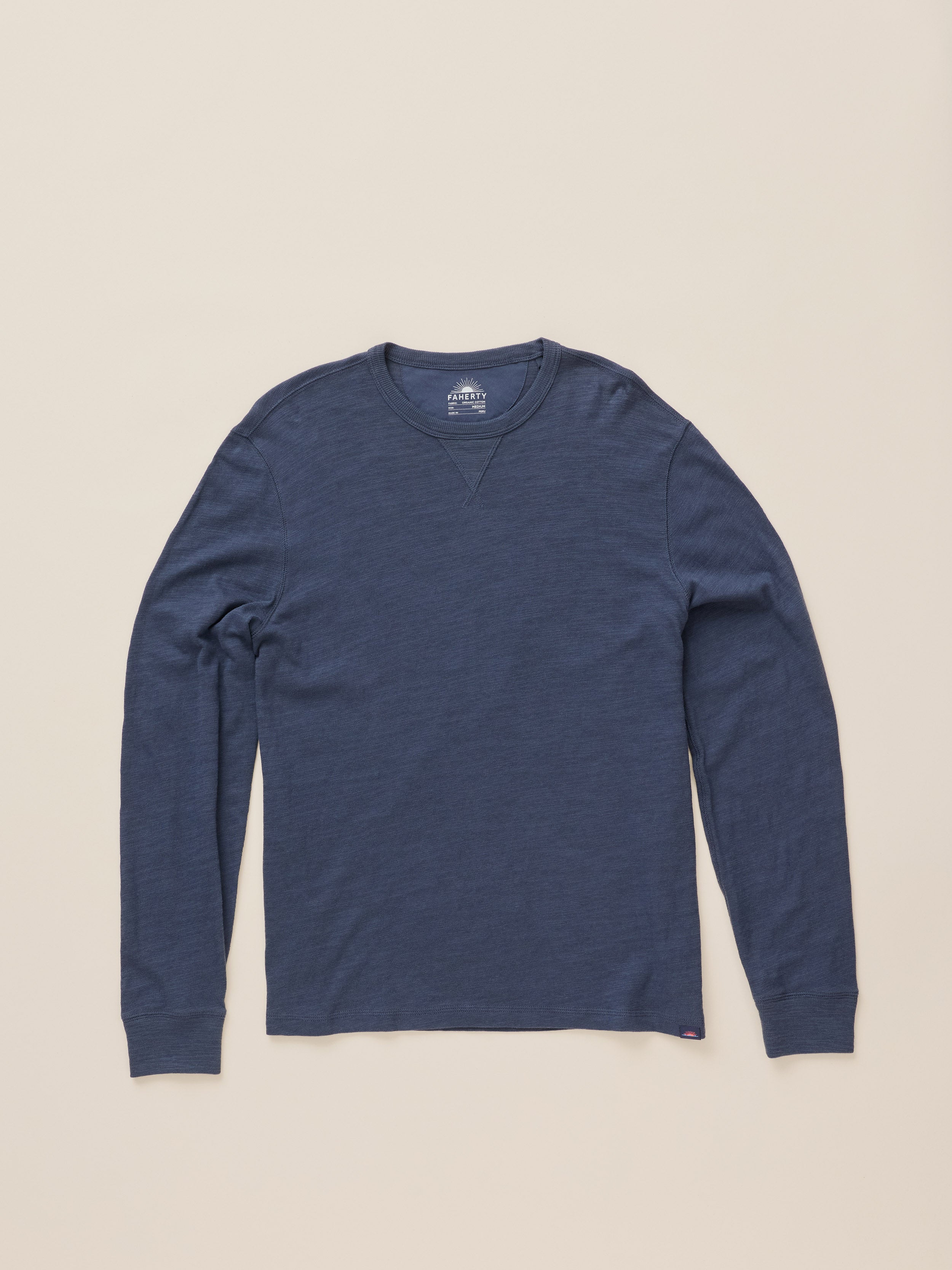 A navy blue long-sleeve crewneck shirt laid flat against a light beige background.