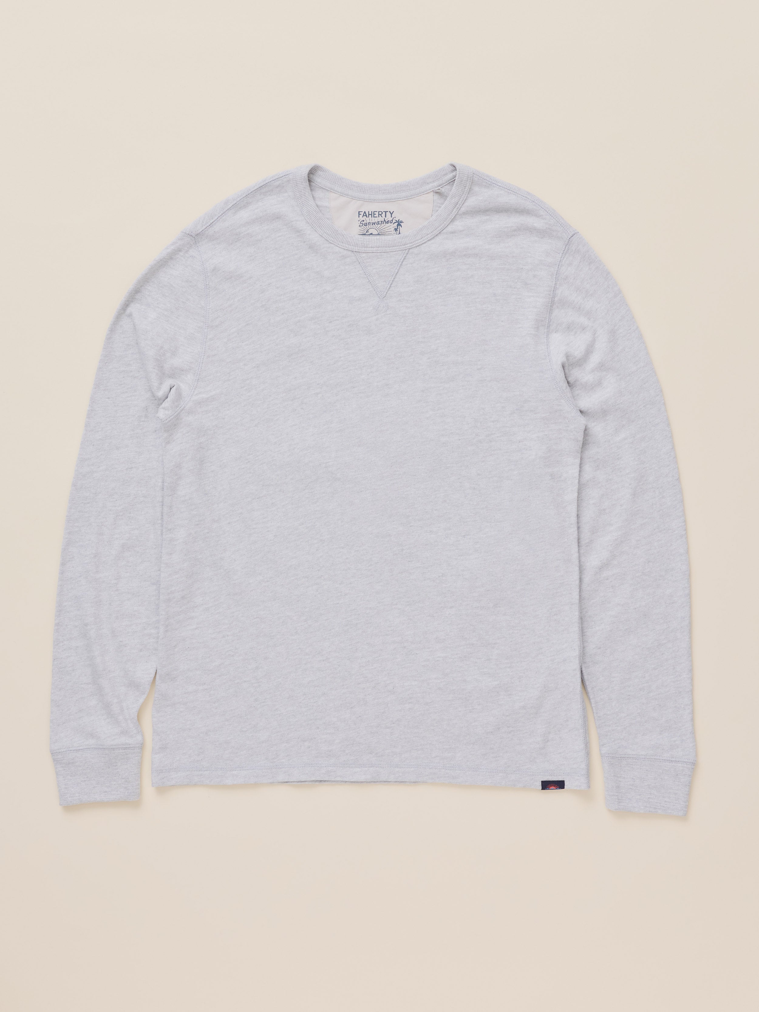 A light gray heather long-sleeve crewneck shirt by Faherty, laid flat against a solid beige background.