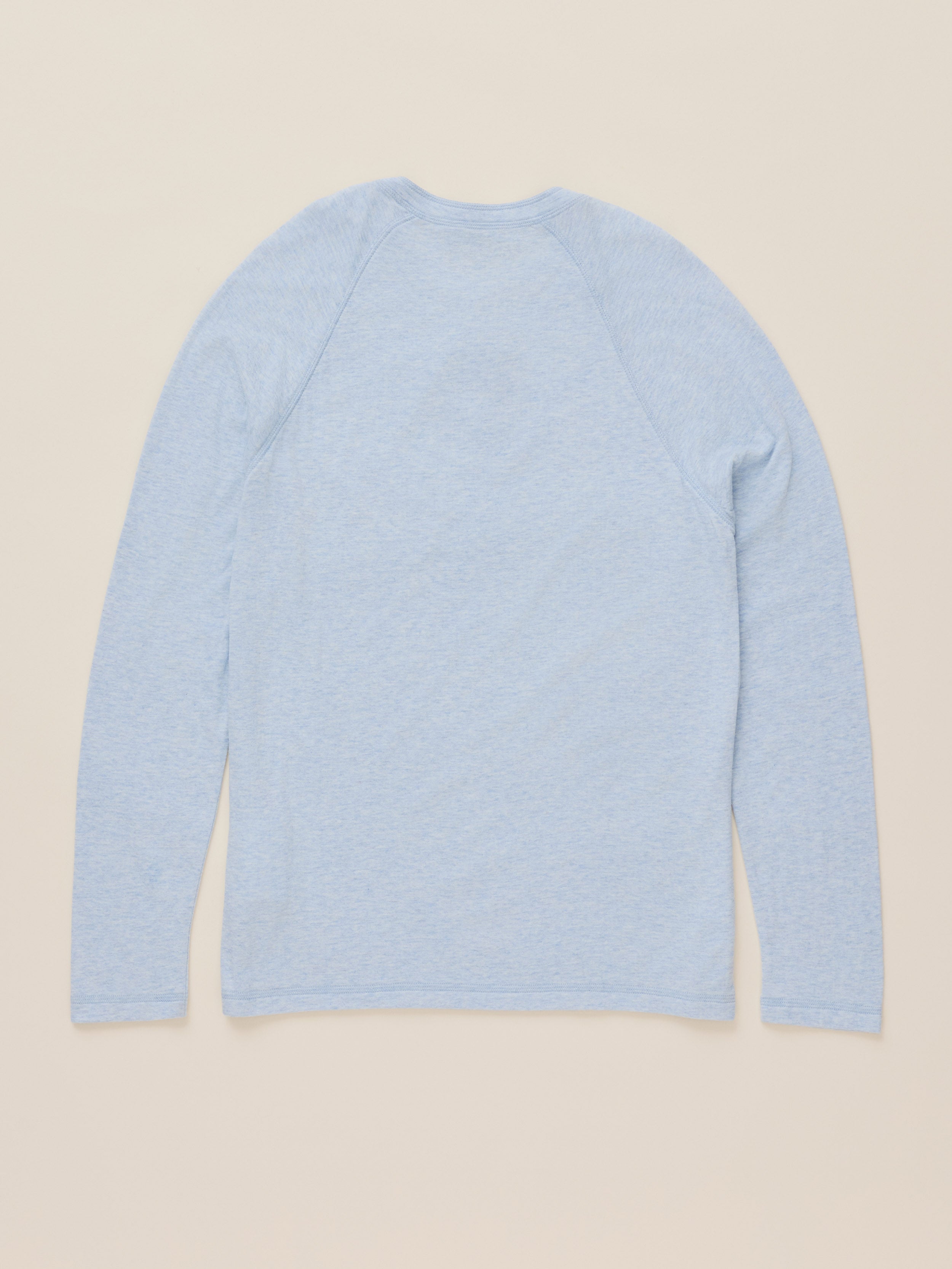 A light blue long-sleeve raglan t-shirt shown from the back, laid flat against a solid beige background.