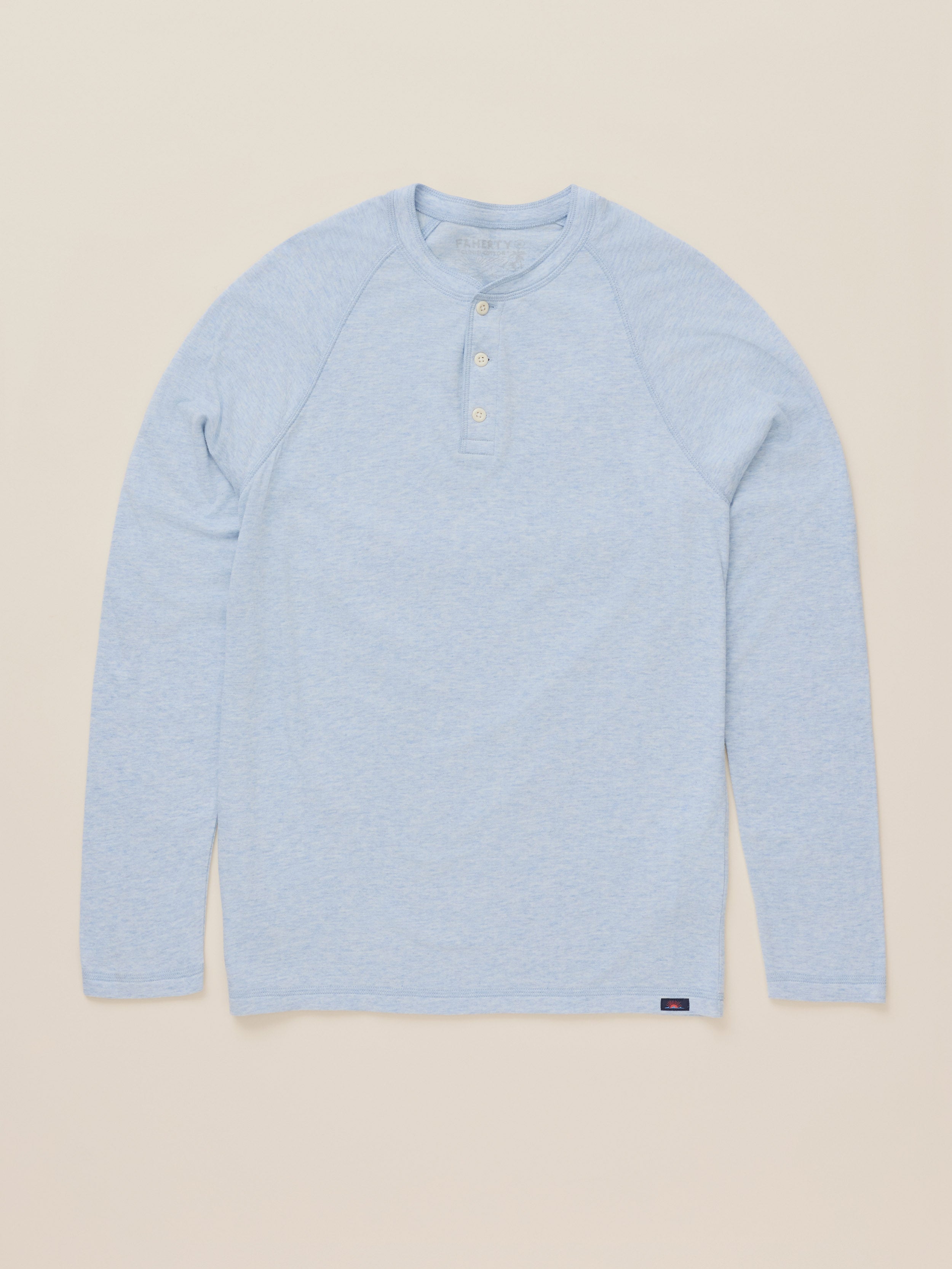A light blue heather long-sleeve henley shirt with a three-button placket, laid flat against a solid beige background.