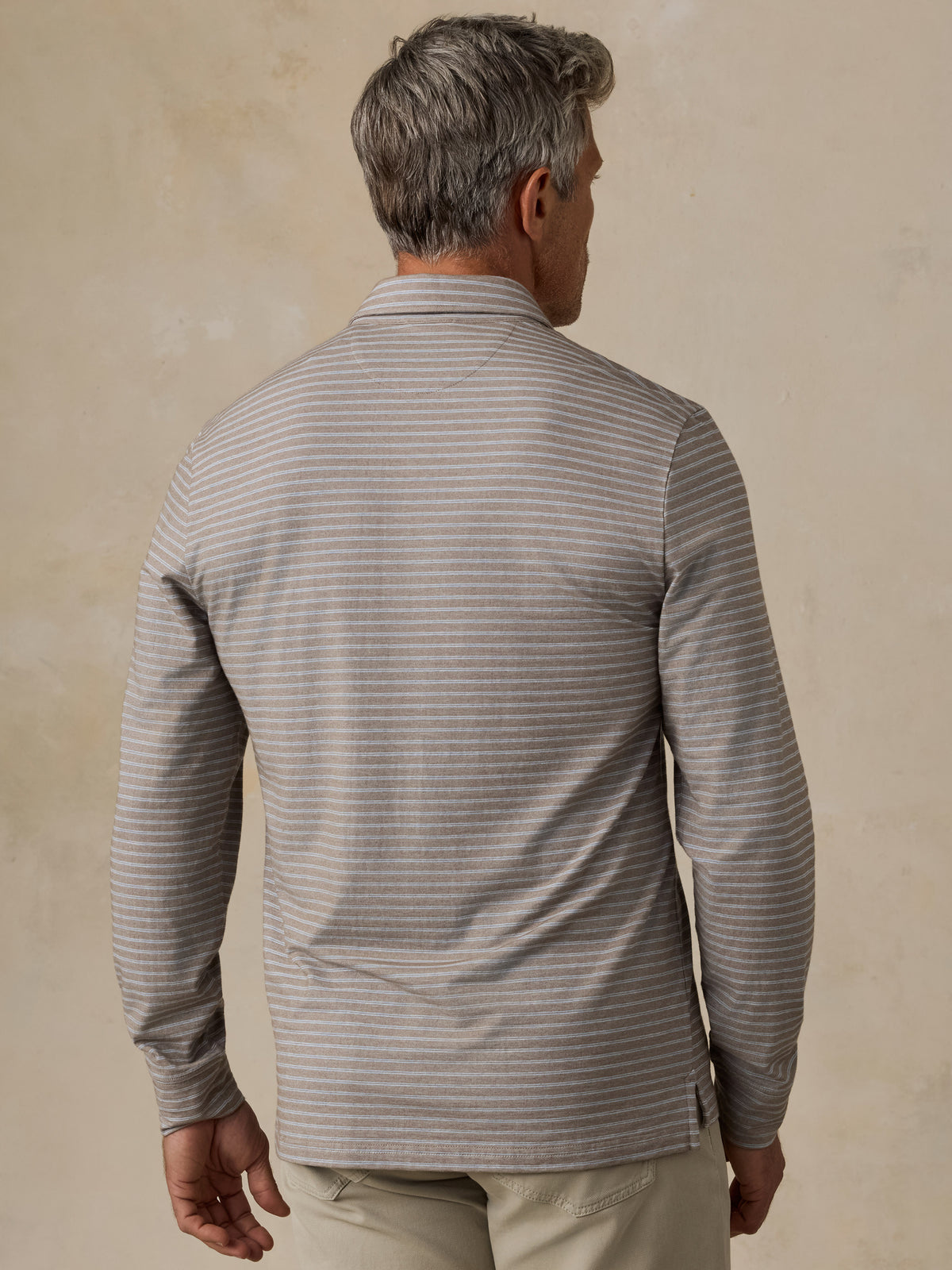 A man viewed from behind wearing a long-sleeve collared polo shirt, khaki pants and a brown belt, image 3 of 6