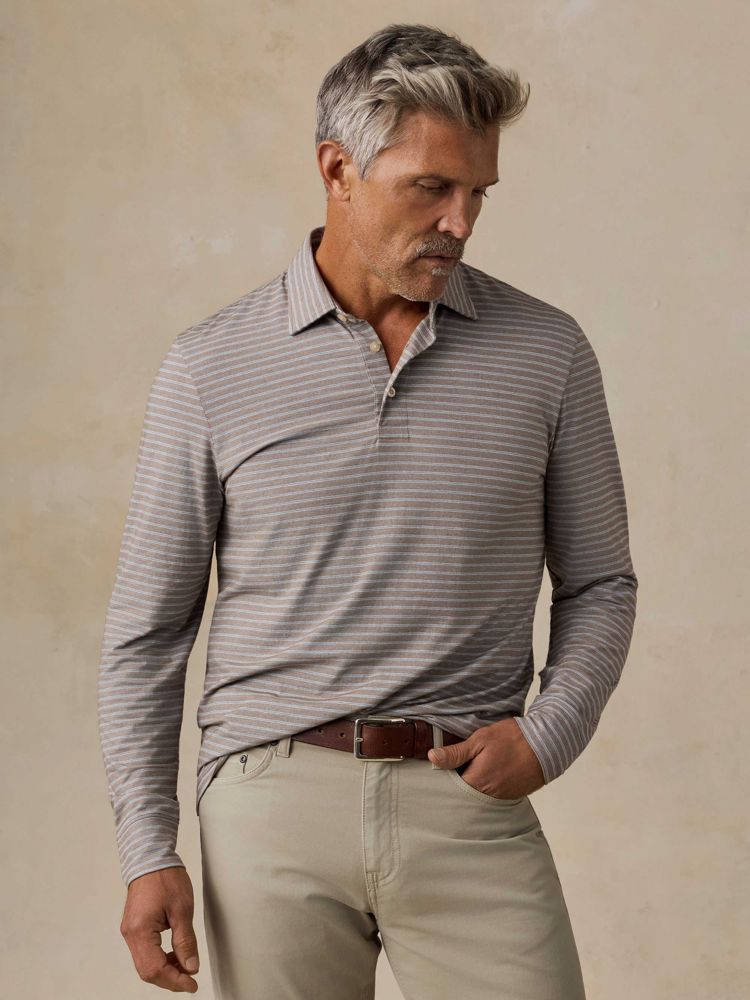 A man wearing a long-sleeve collared polo shirt, khaki pants and a brown belt
