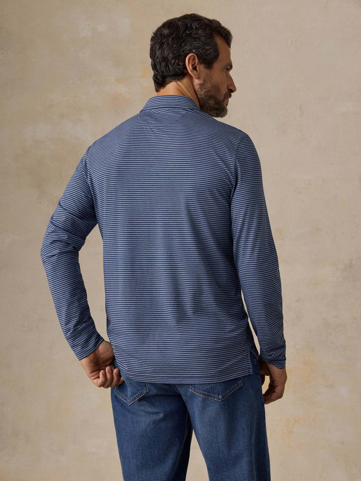 A man viewed from behind wearing a blue striped polo shirt and blue jeans, image 5 of 5