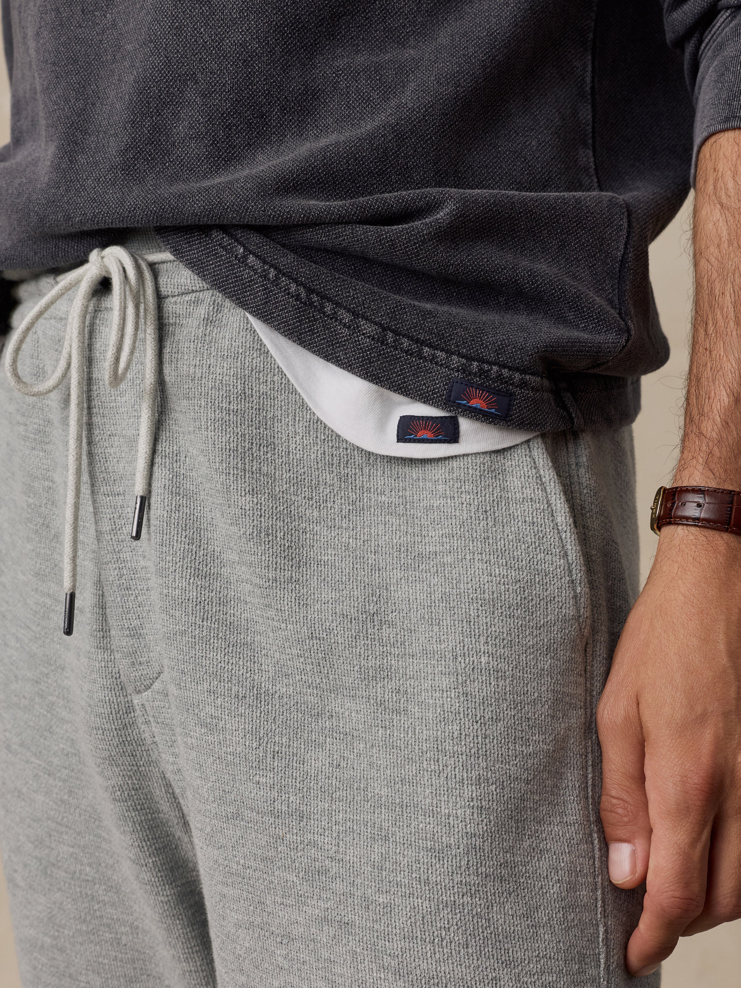 Close-up of a person wearing heather gray drawstring sweatpants and a dark charcoal top, with a small visible Faherty brand logo patch near the hem.