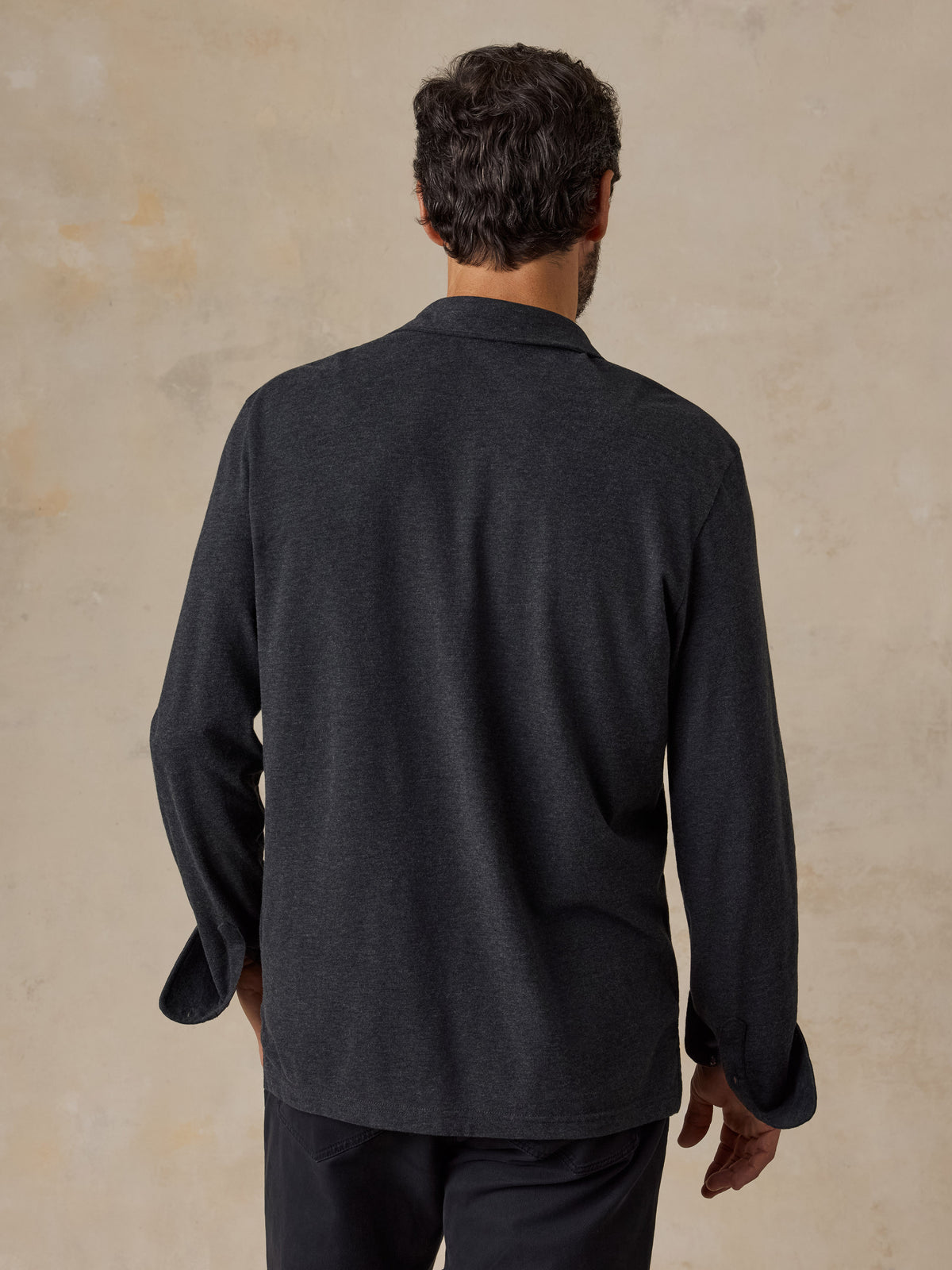 A man viewed from behind wearing a dark grey sweater polo and black chino pants, image 2 of 6