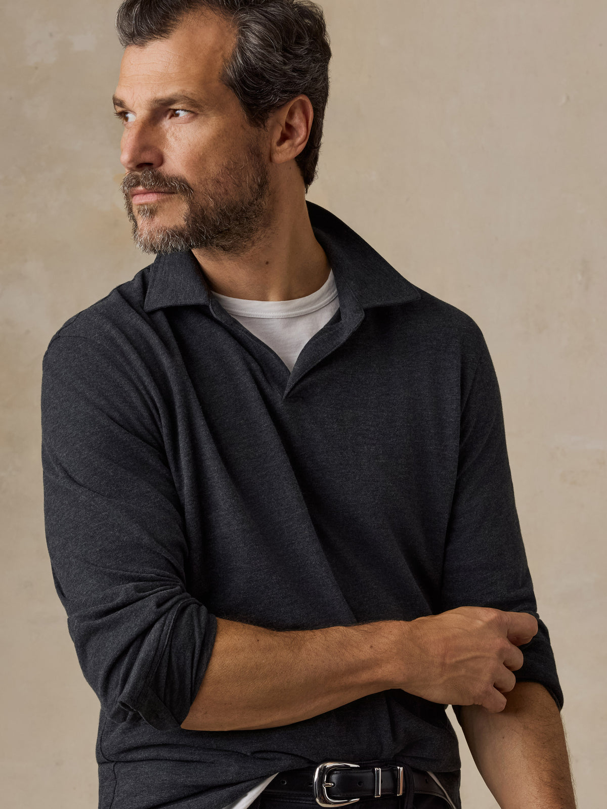 A man wearing a dark grey sweater polo and black chino pants, image 4 of 6
