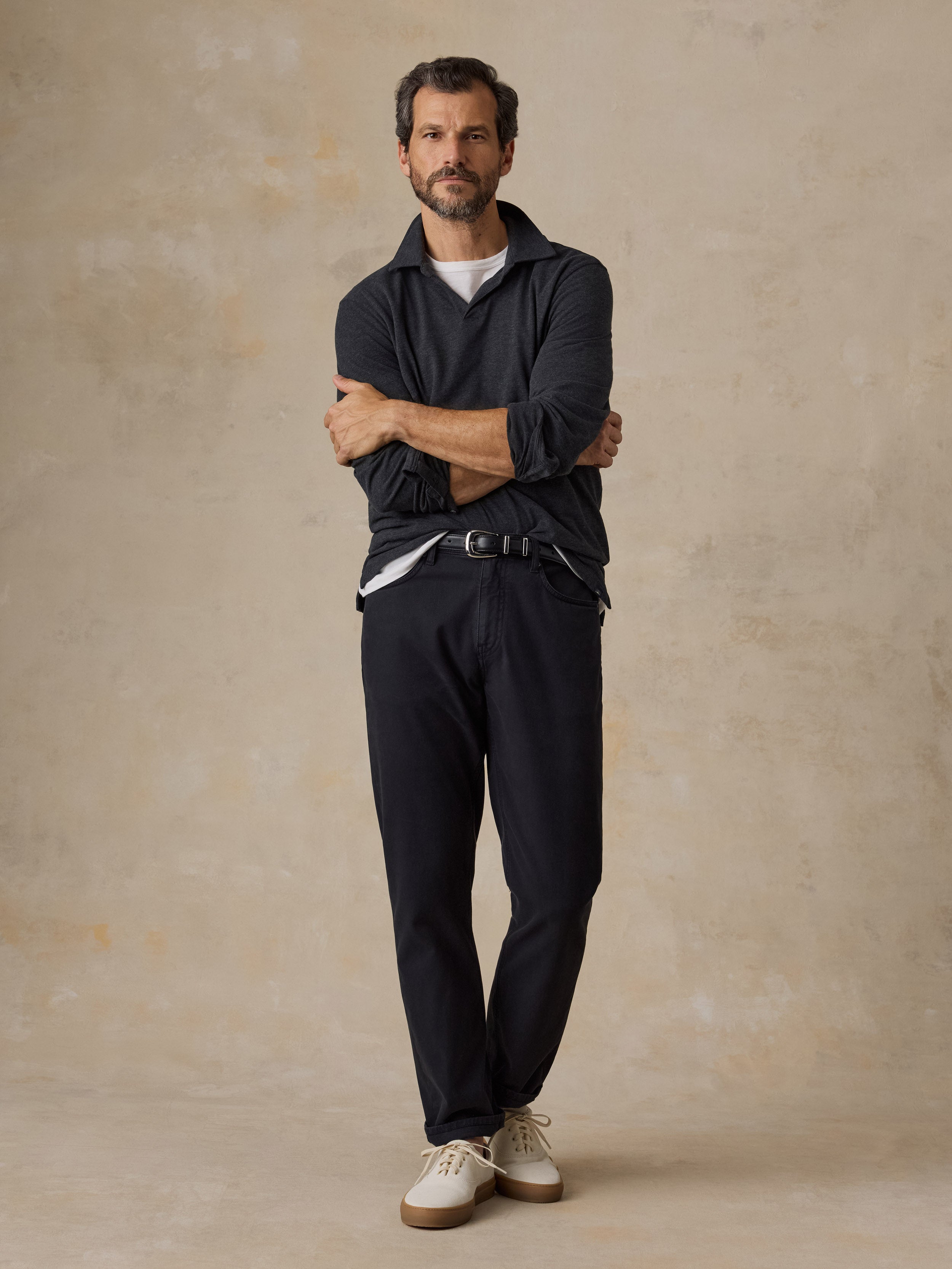 A man wearing a dark grey sweater polo, black chino pants, and white sneakers