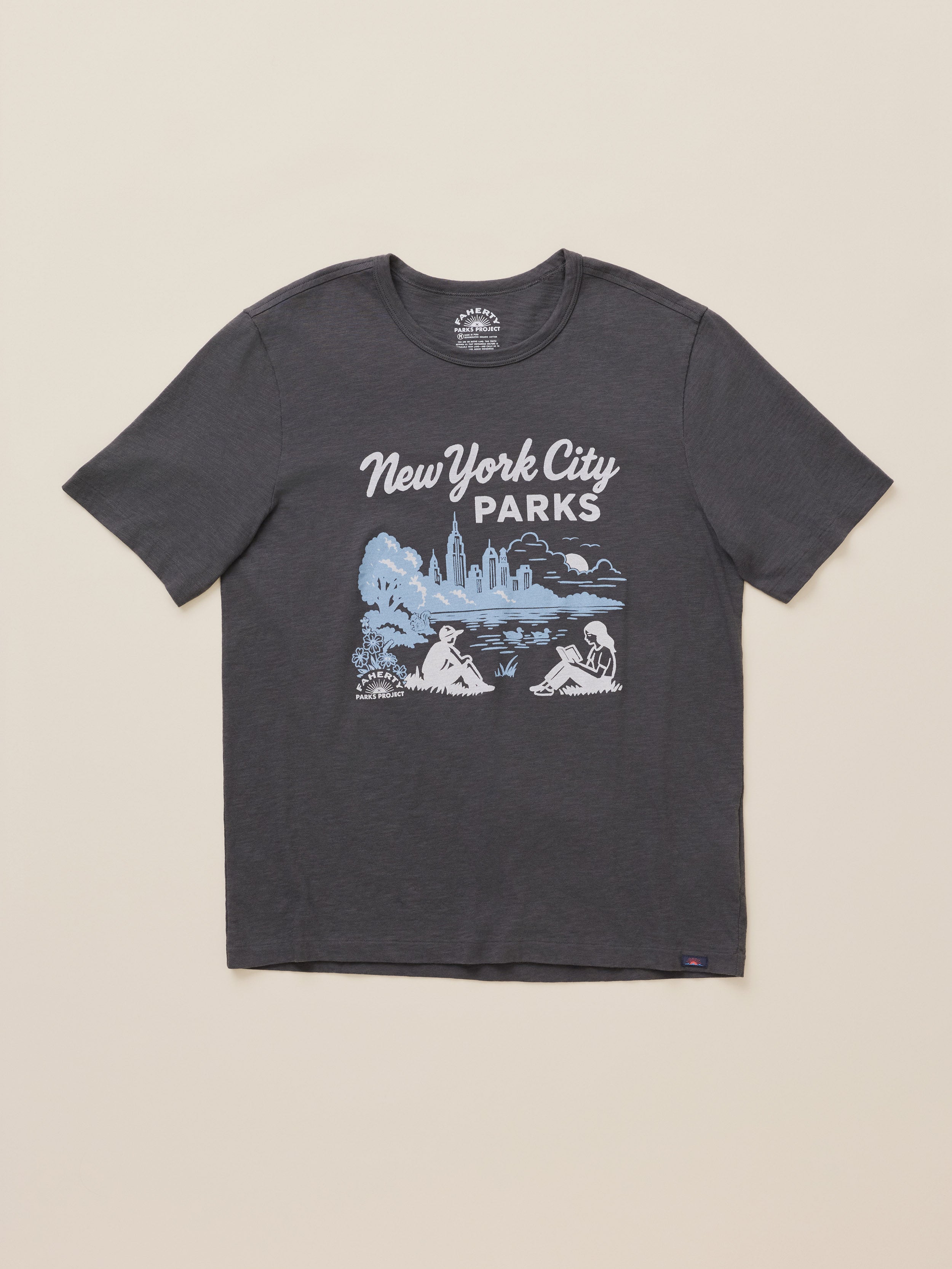 A dark charcoal gray short-sleeve t-shirt with a light blue and white graphic print reading 'New York City Parks' and showing a scenic illustration, laid flat on a light beige background.