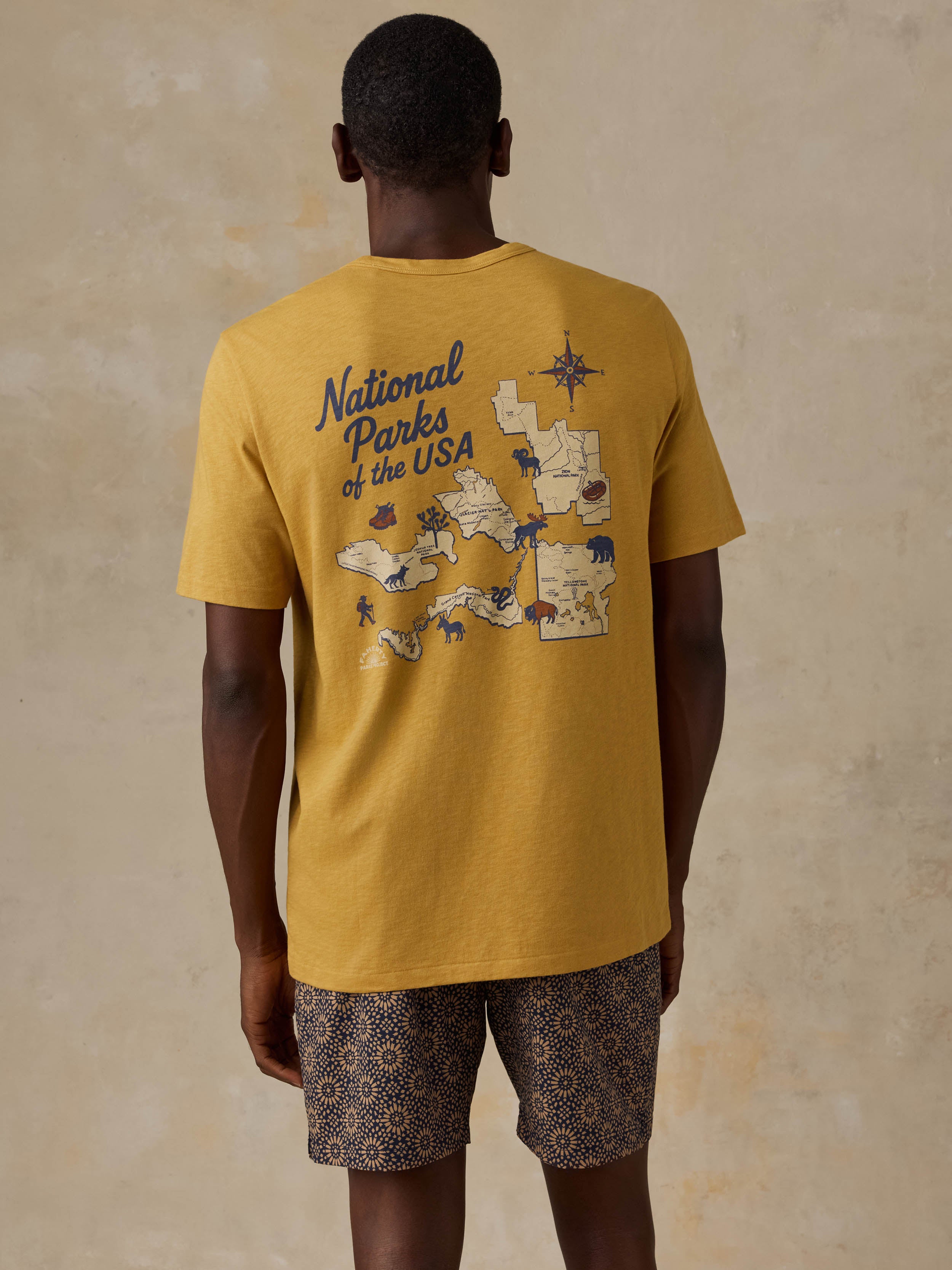 A man wearing a yellow National Parks tee with printed shorts against a beige background