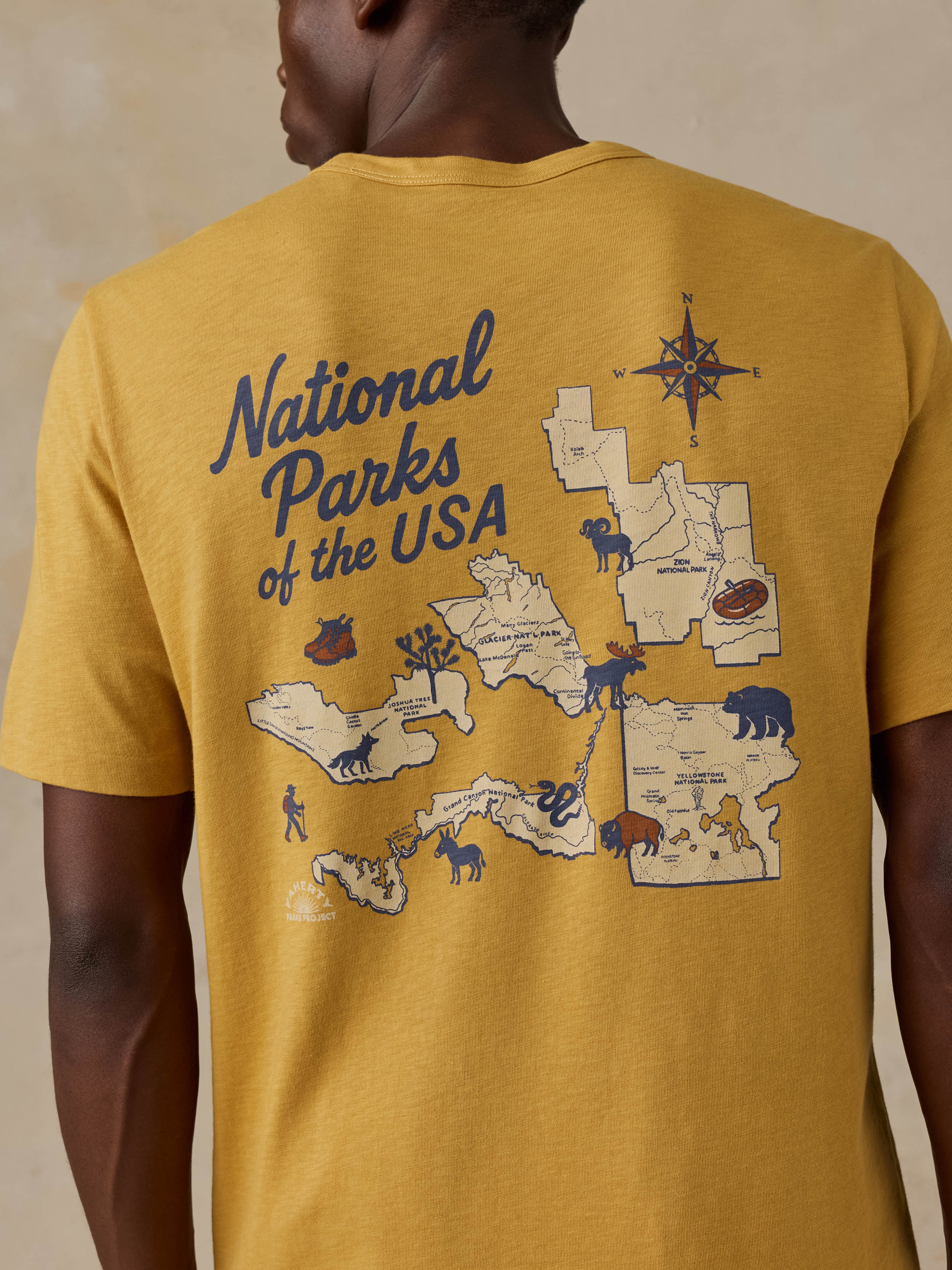 A man wearing a yellow National Parks tee against a beige background