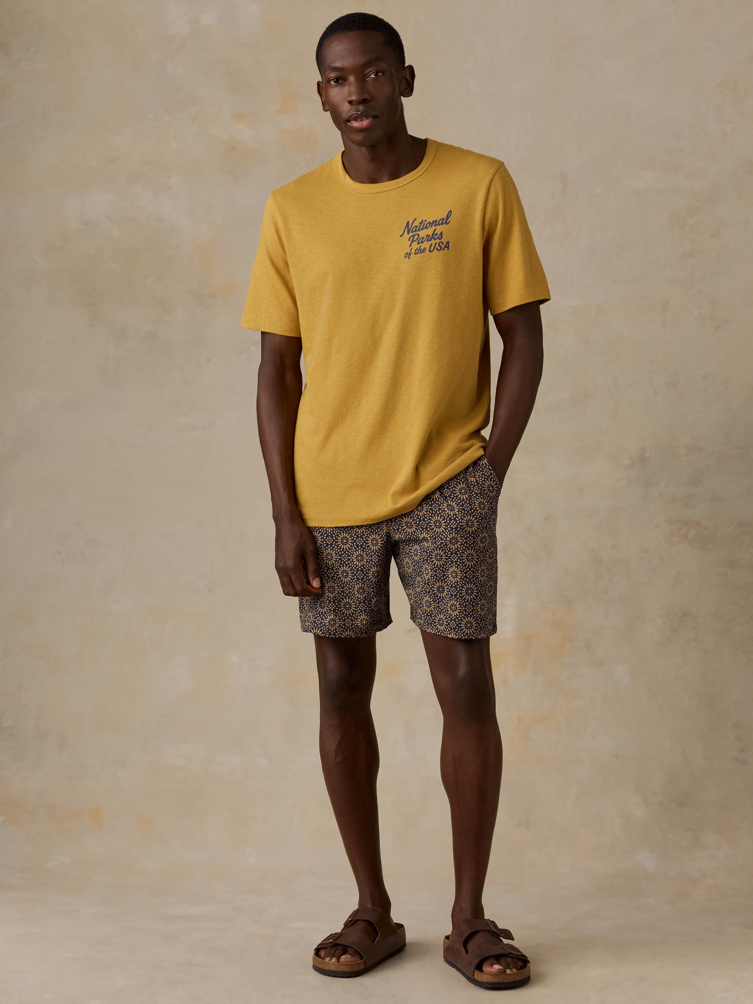 A man wearing a yellow National Parks tee with printed shorts against a beige background