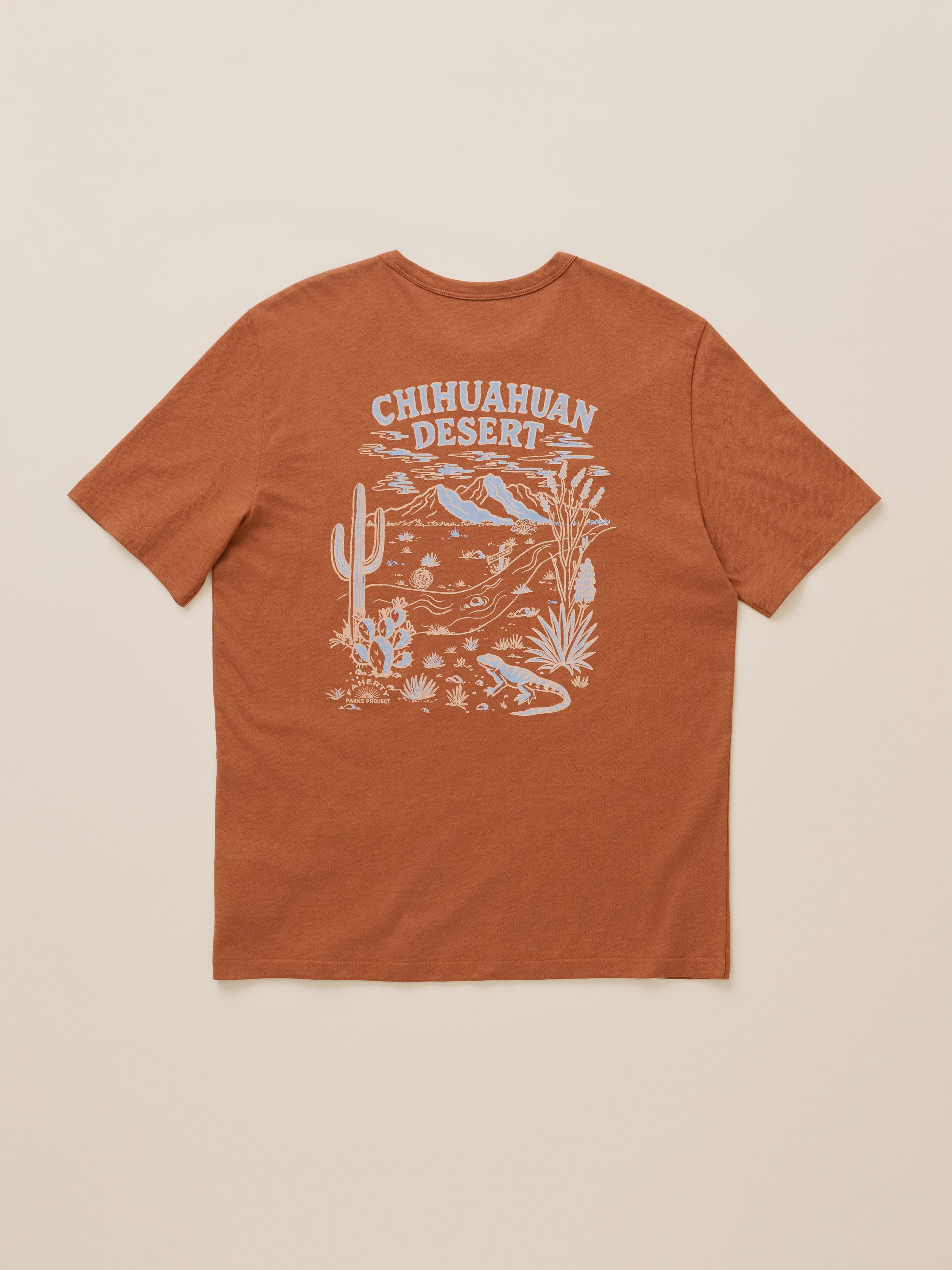 A rust-orange short-sleeve t-shirt shown from the back, featuring a white graphic print of a desert landscape with a saguaro cactus, birds, and the text 'Chihuahuan Desert'.