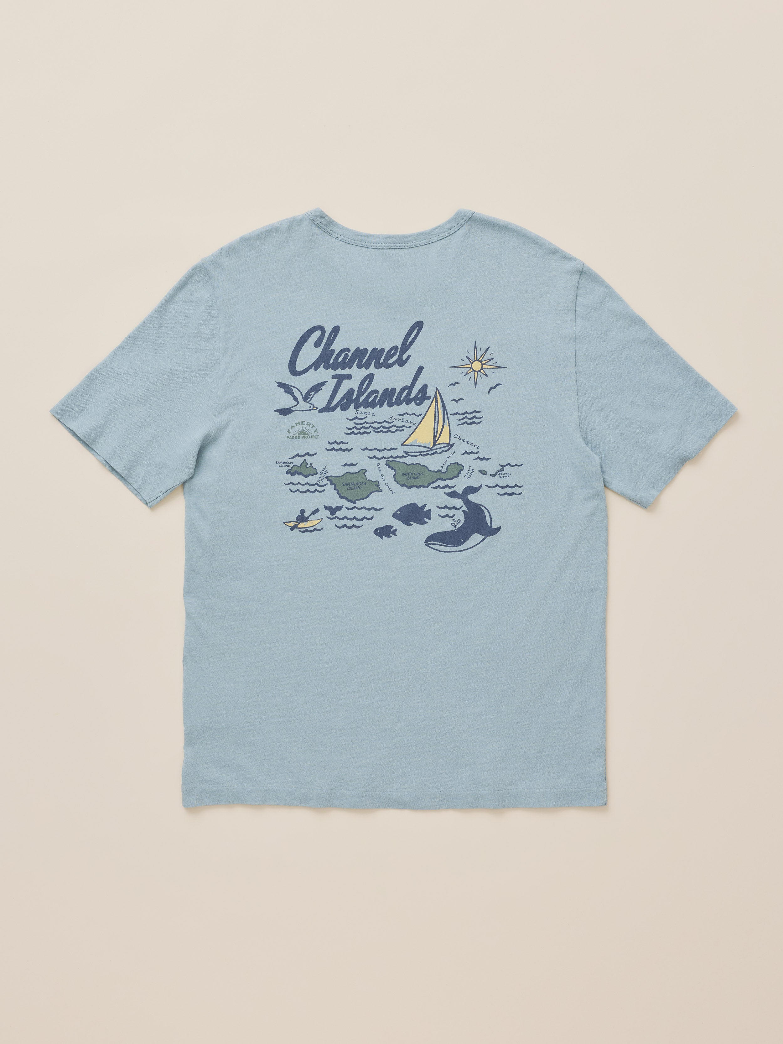 A light blue short-sleeve t-shirt with a 'Channel Islands' nautical graphic on the front, featuring a sailboat, whales, and stars, displayed flat against a light beige background.