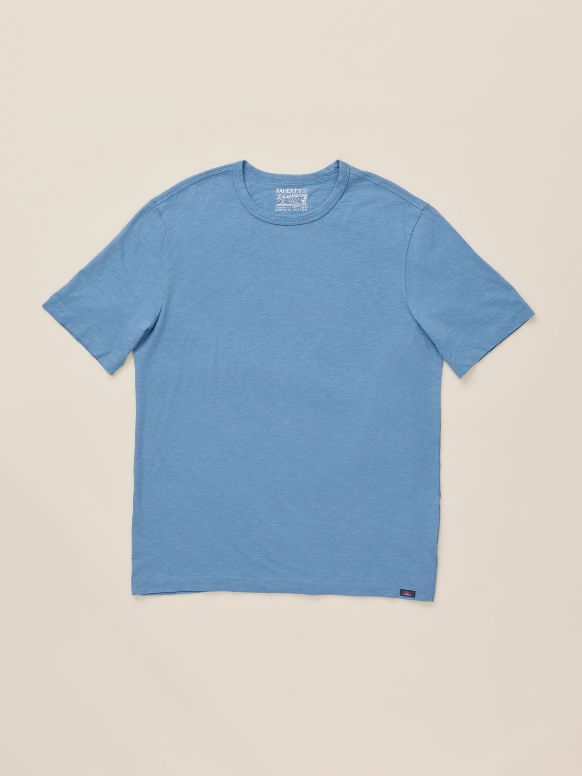 A light blue short-sleeve crewneck t-shirt laid flat against a solid beige background., image 6 of 7