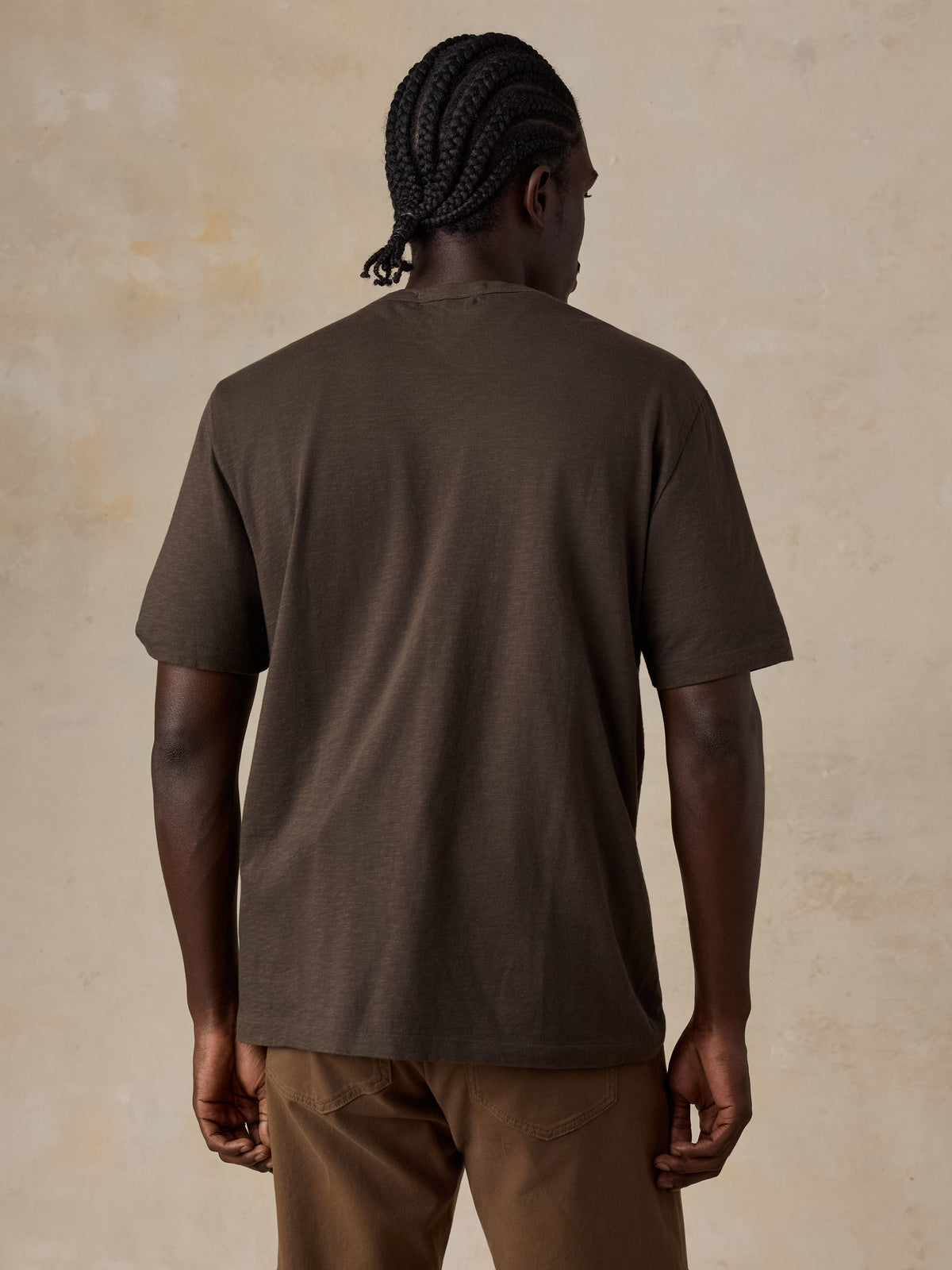 A man viewed from the back wearing a brown t-shirt and brown pants, image 2 of 6