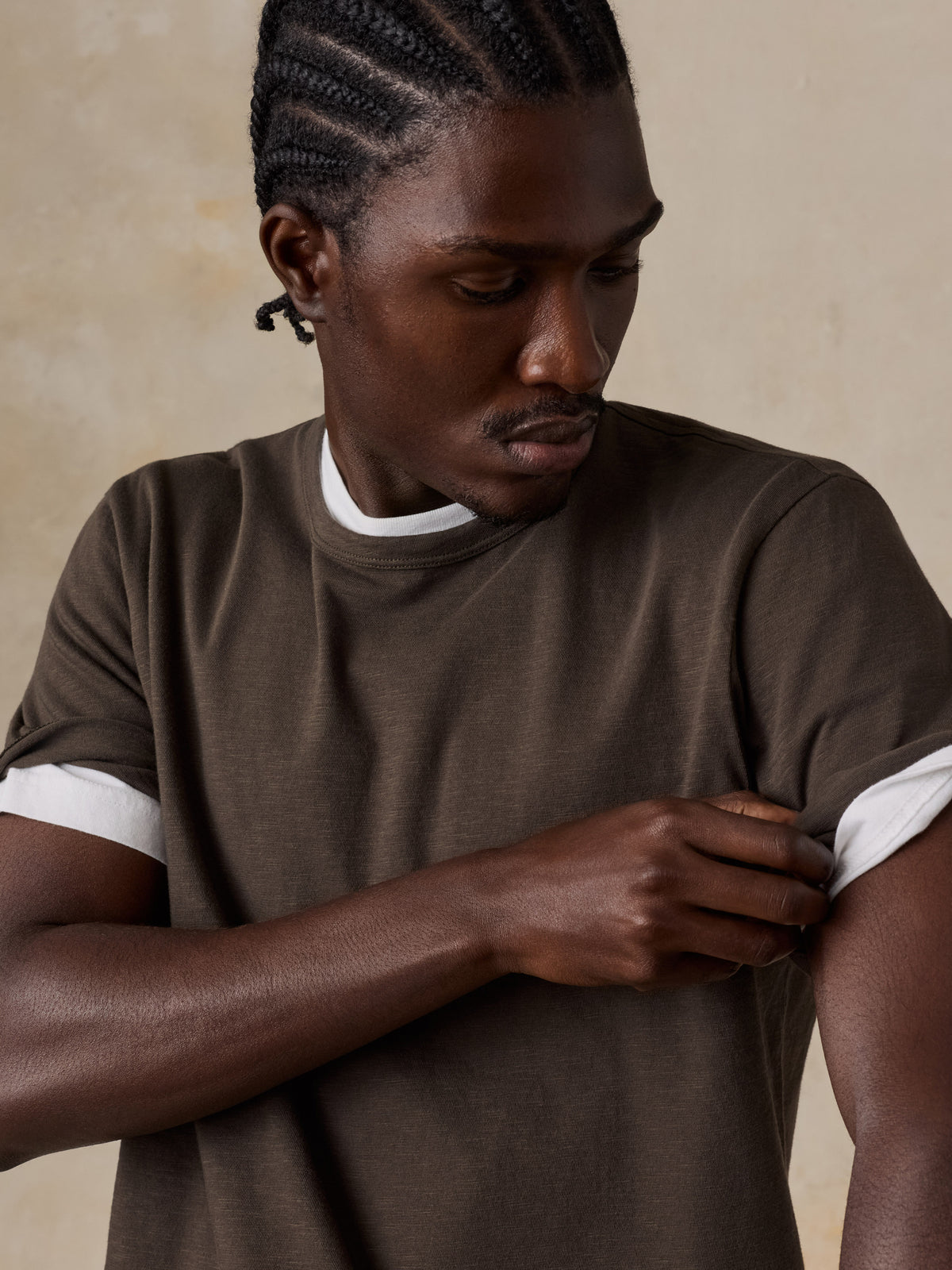 A man wearing a brown t-shirt over a white t-shirt, image 5 of 6