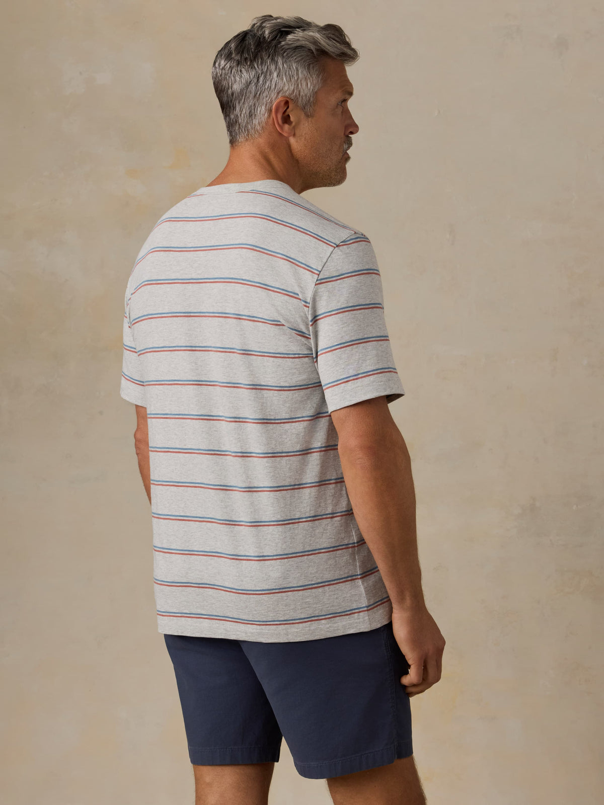 Man wearing a striped t-shirt and navy shorts against a beige background, image 3 of 5