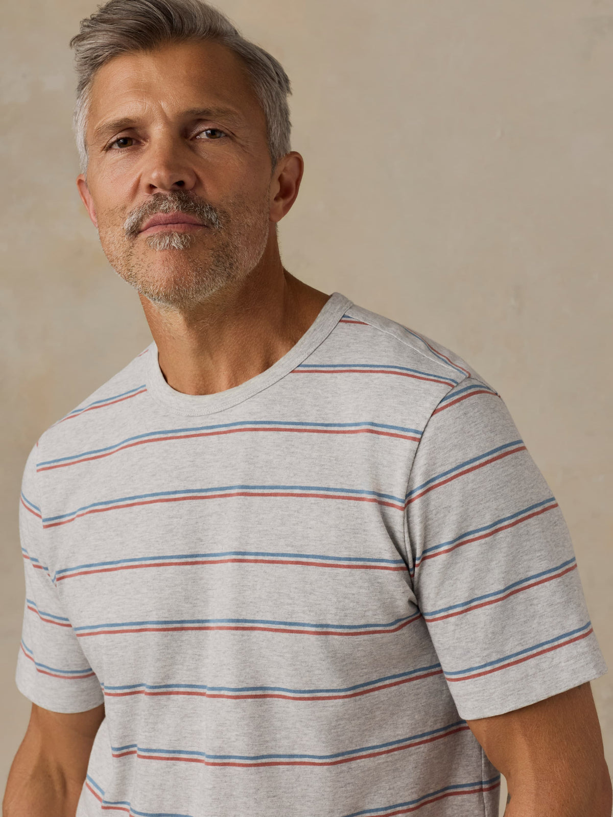 Man wearing a gray striped t-shirt against a beige background, image 4 of 5