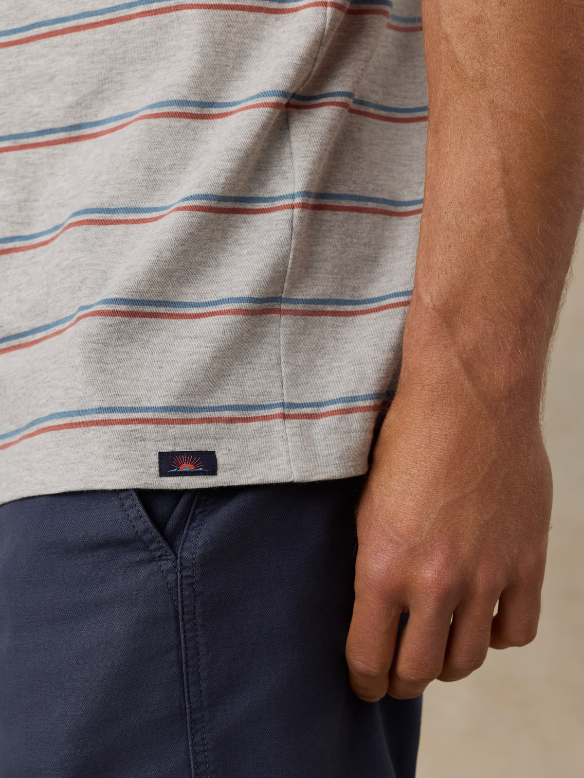 Close-up of a man wearing a striped shirt with a Faherty brand logo and navy shorts on a beige background, image 5 of 5