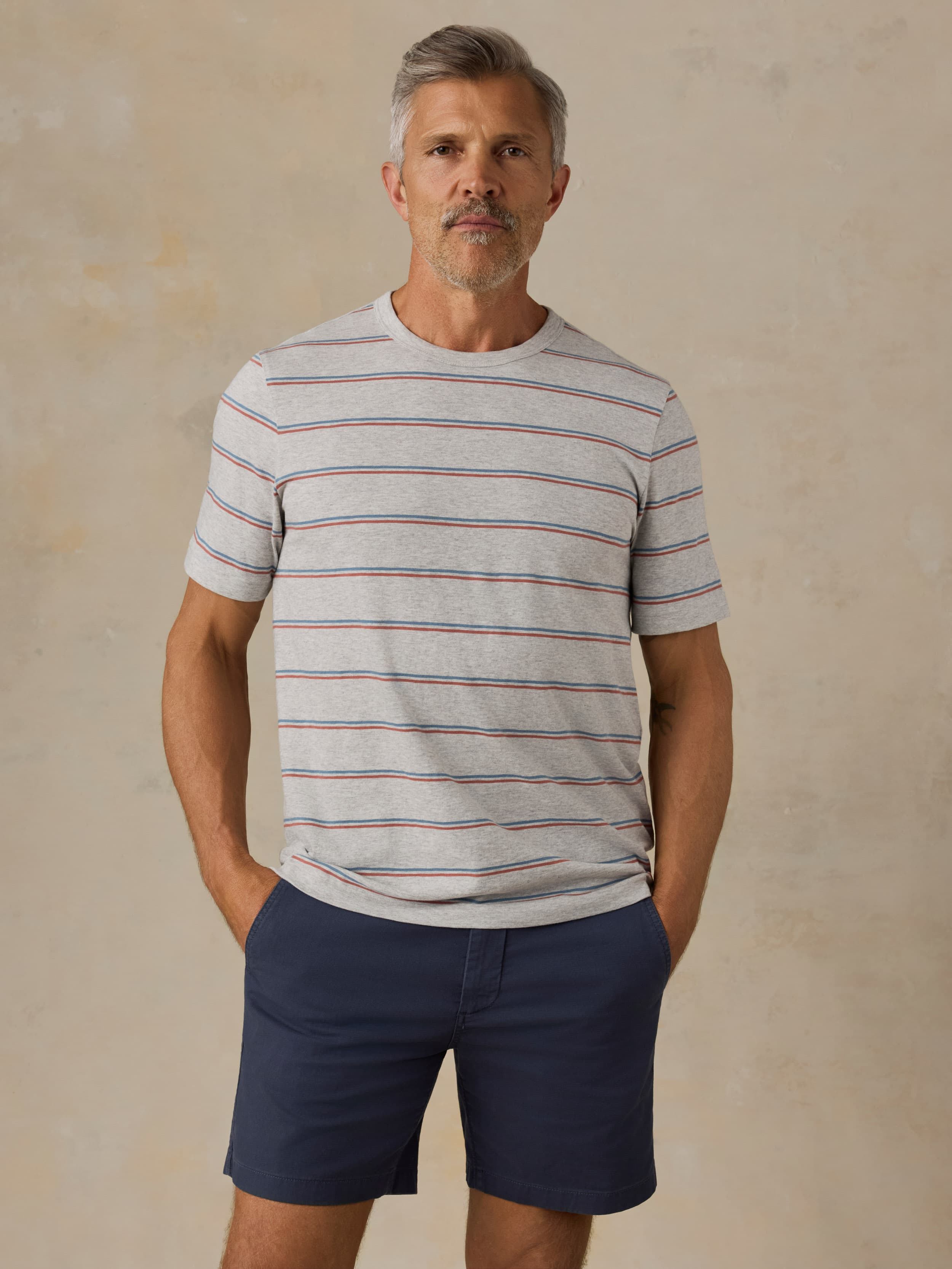 Man wearing a striped shirt and navy shorts against a beige background
