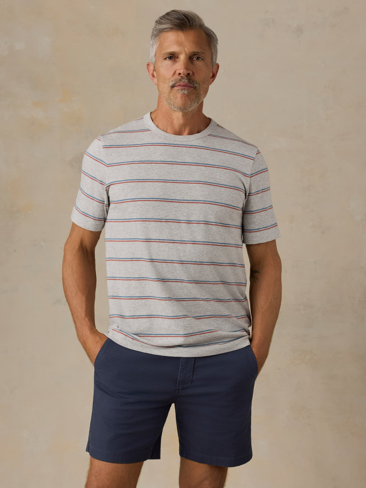 Man wearing a striped shirt and navy shorts against a beige background, image 1 of 5