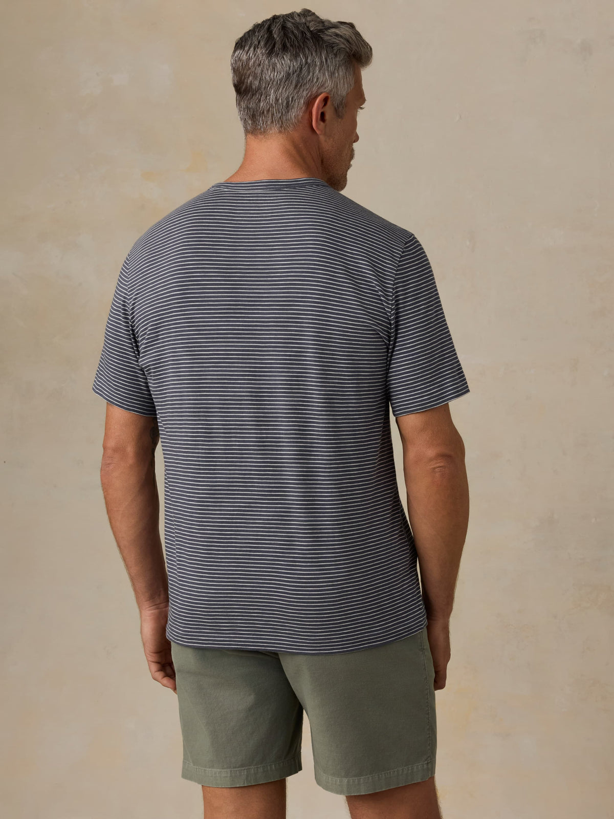 Man wearing a striped shirt and shorts against a beige background, image 4 of 5