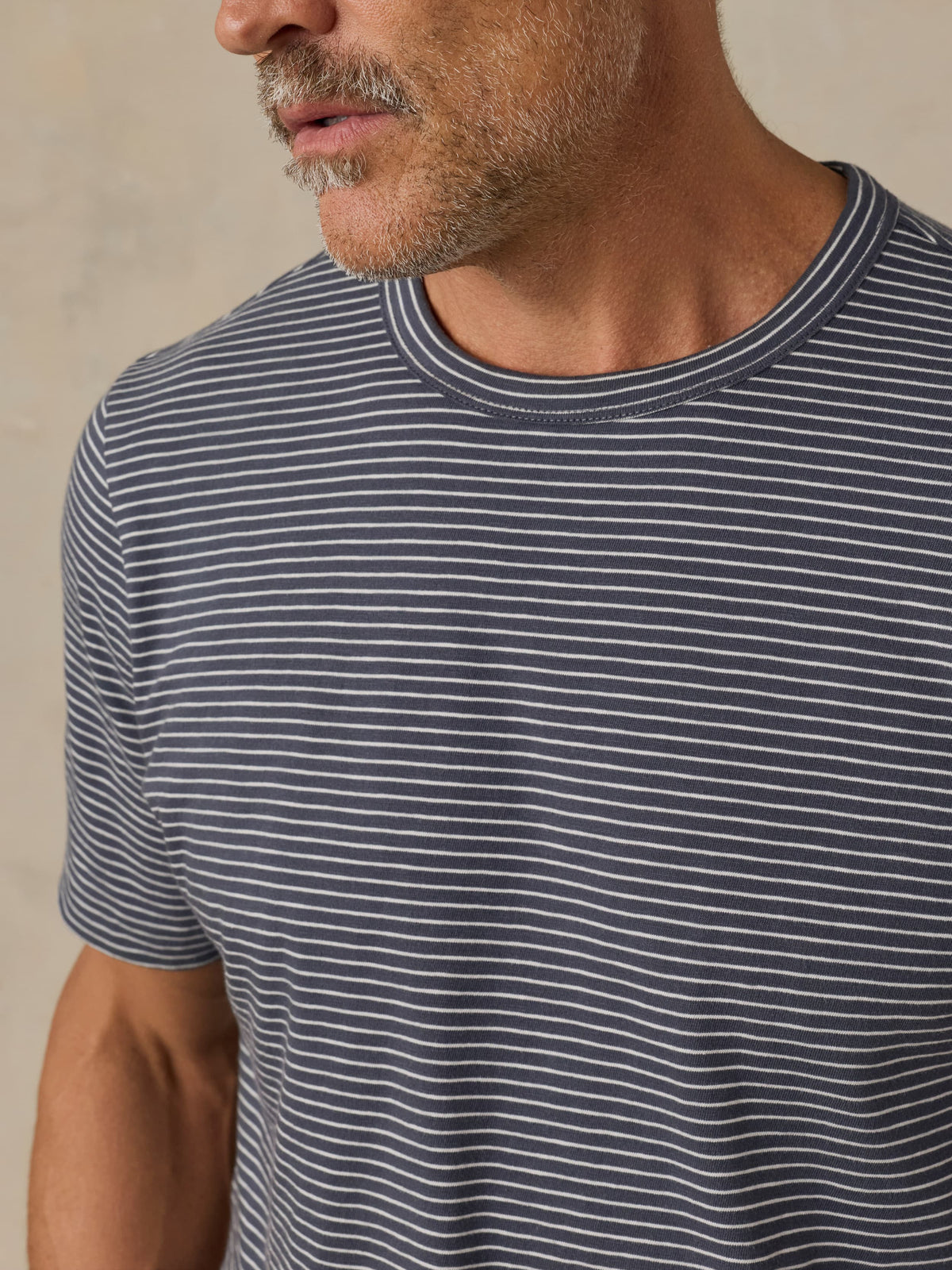 Man wearing a blue and white striped t-shirt against a beige background, image 3 of 5
