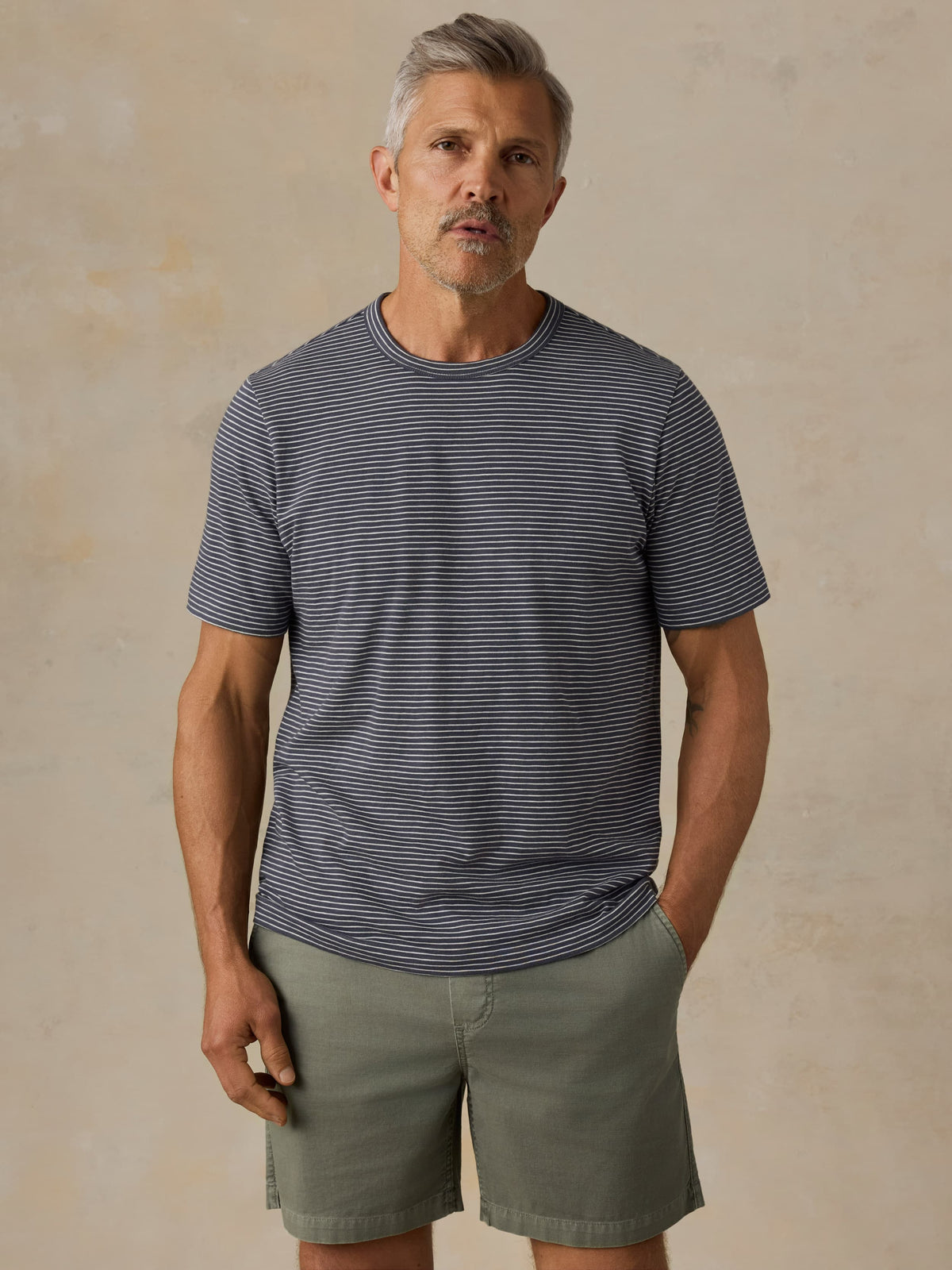 Man wearing blue striped shirt and green shorts against a beige background, image 1 of 5