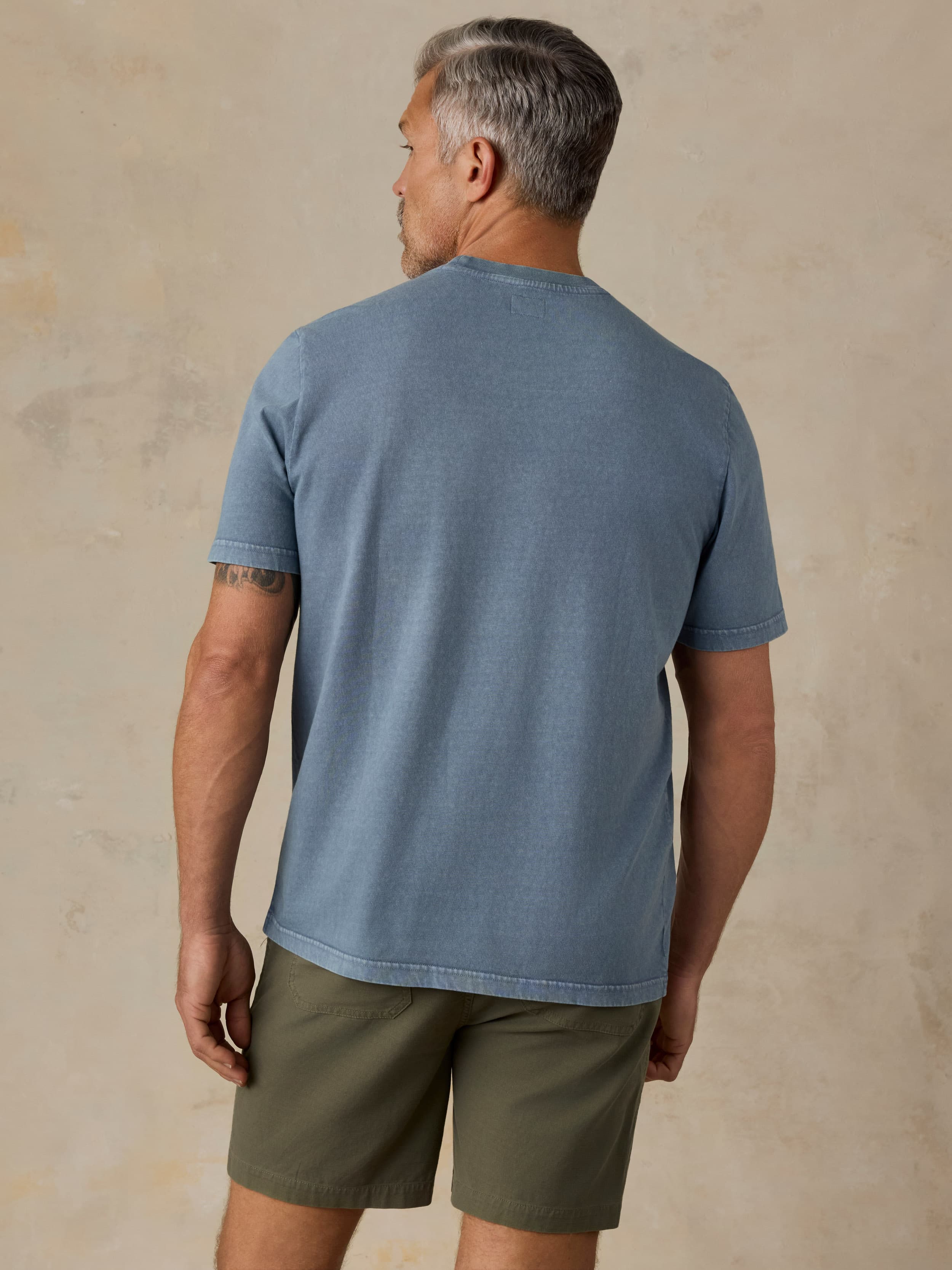 Man wearing a blue pocket tee and green shorts against a beige background