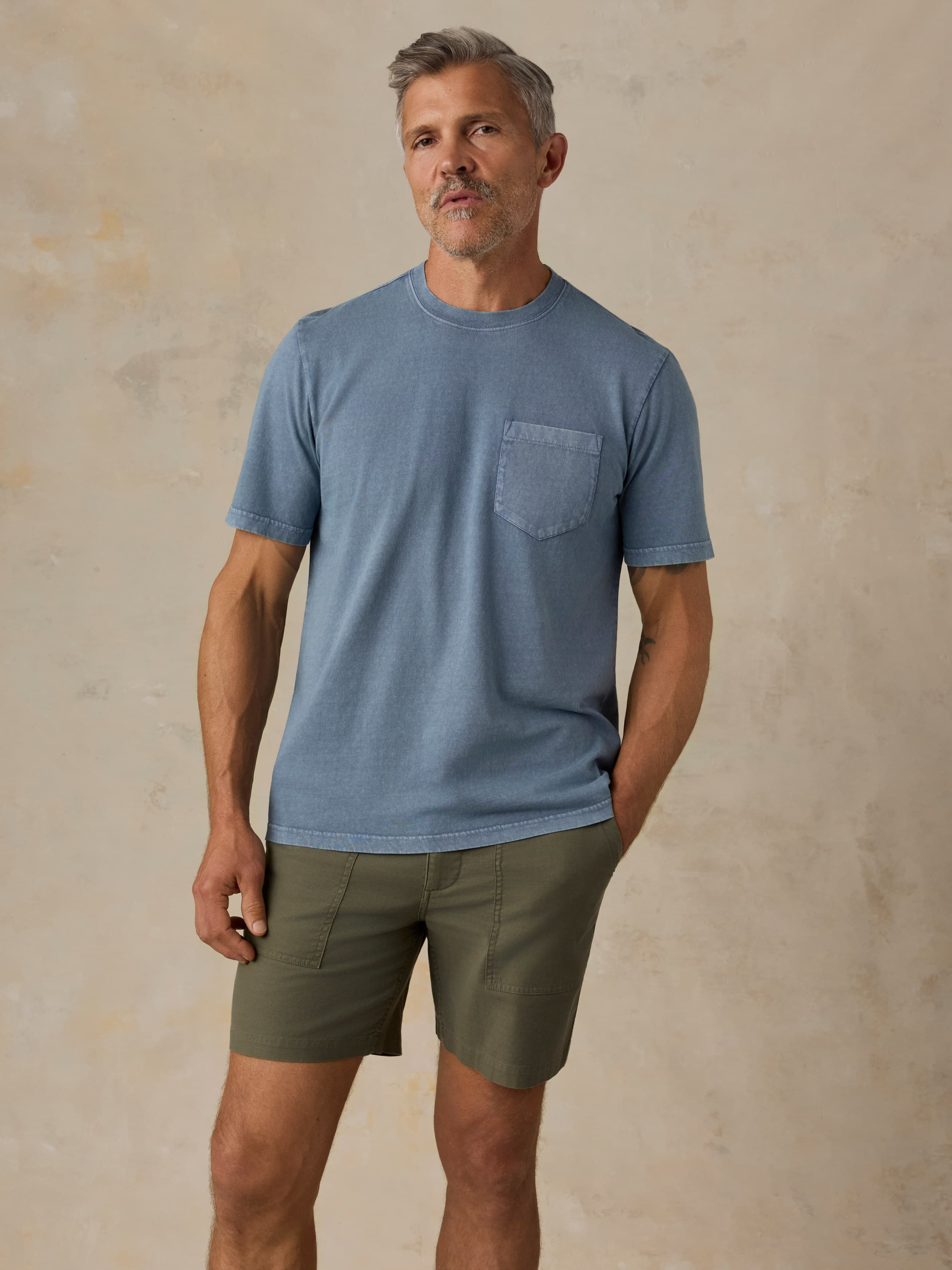 Man wearing a blue pocket tee and green shorts against a beige background