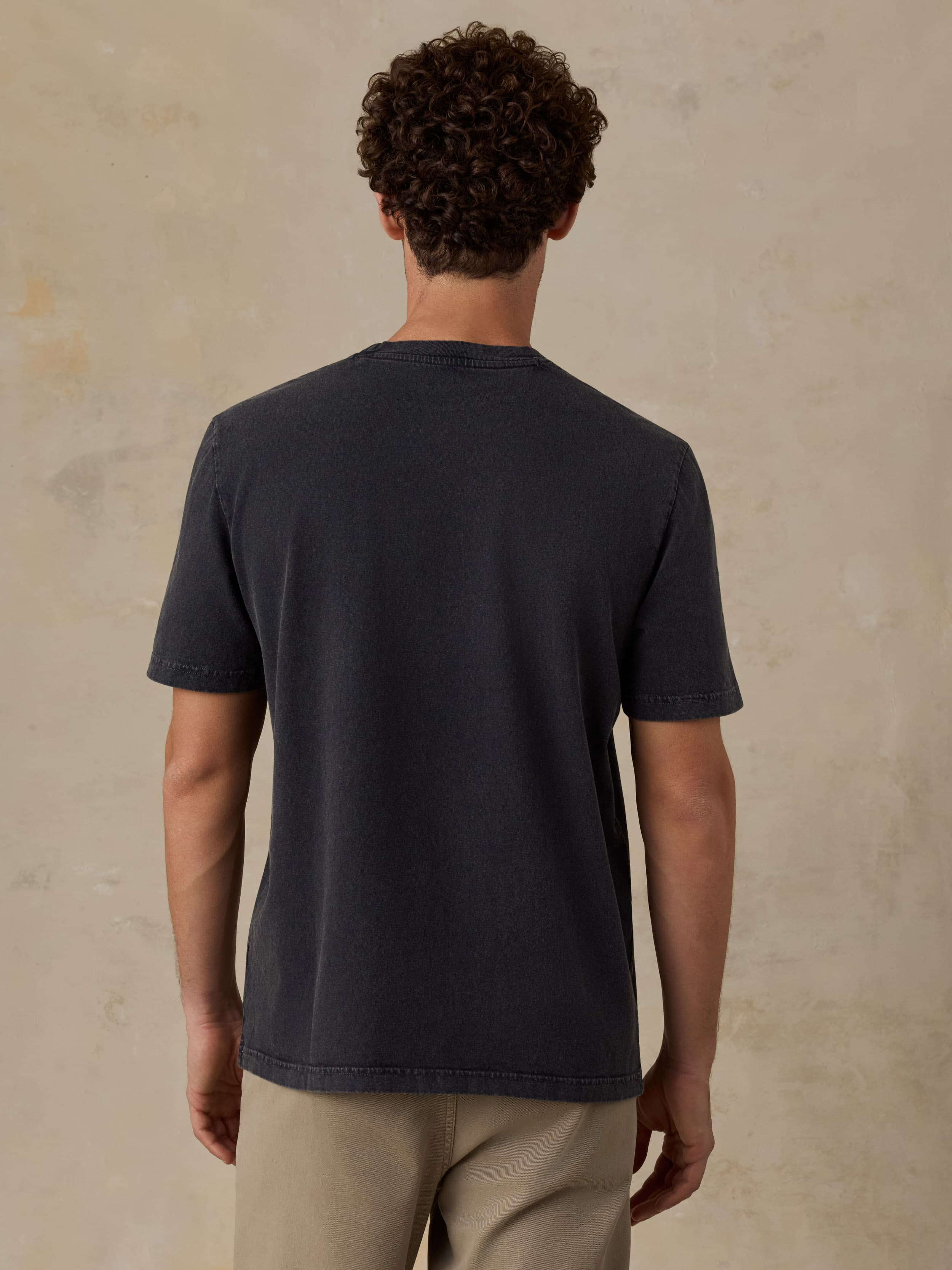 Person wearing a black t-shirt against a beige wall