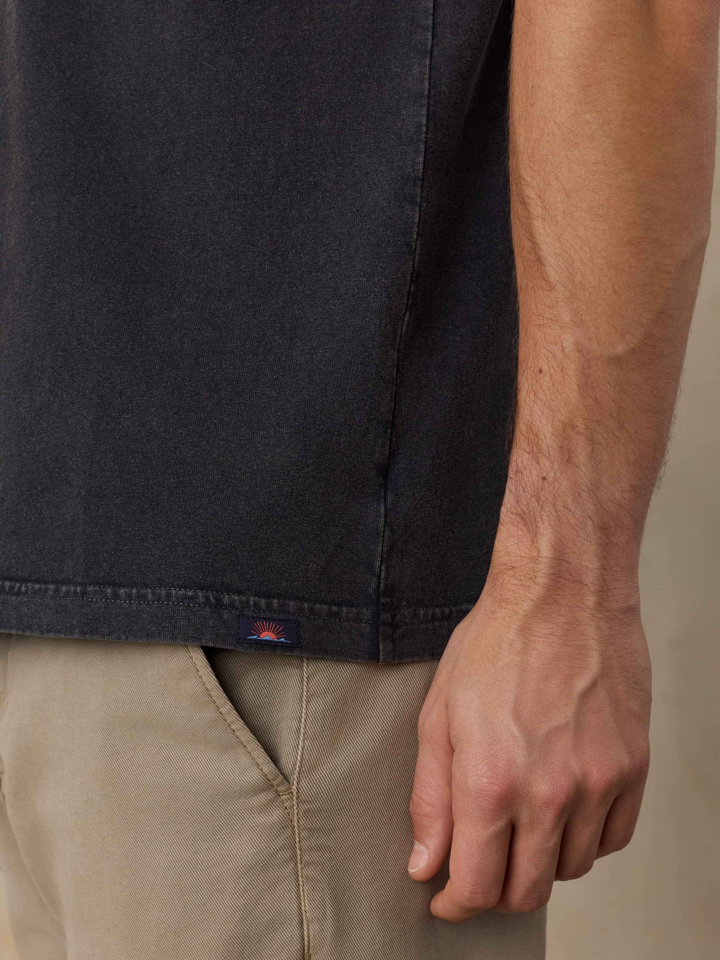 Close-up of a man wearing a dark shirt and beige pants with a visible Faherty brand logo.