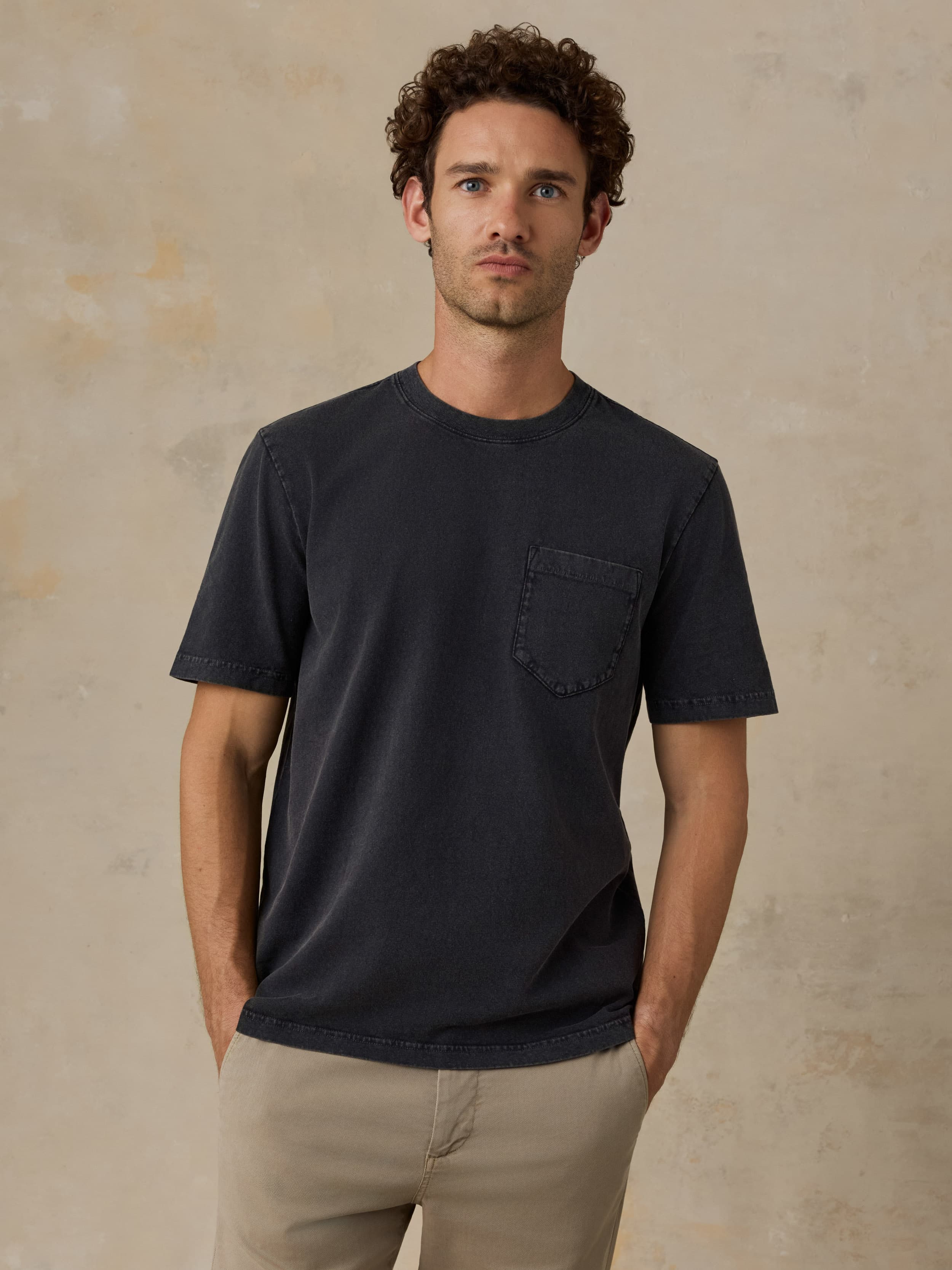 Man wearing a black t-shirt with a pocket against a beige background