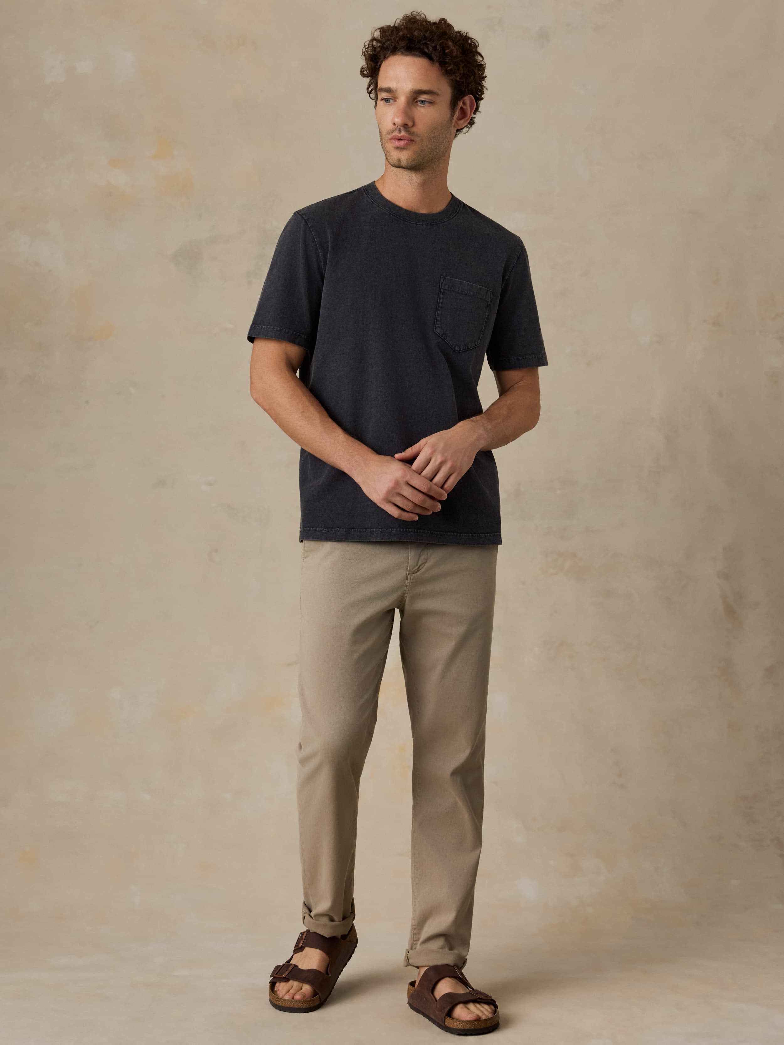 Man wearing a black t-shirt and beige pants against a beige background