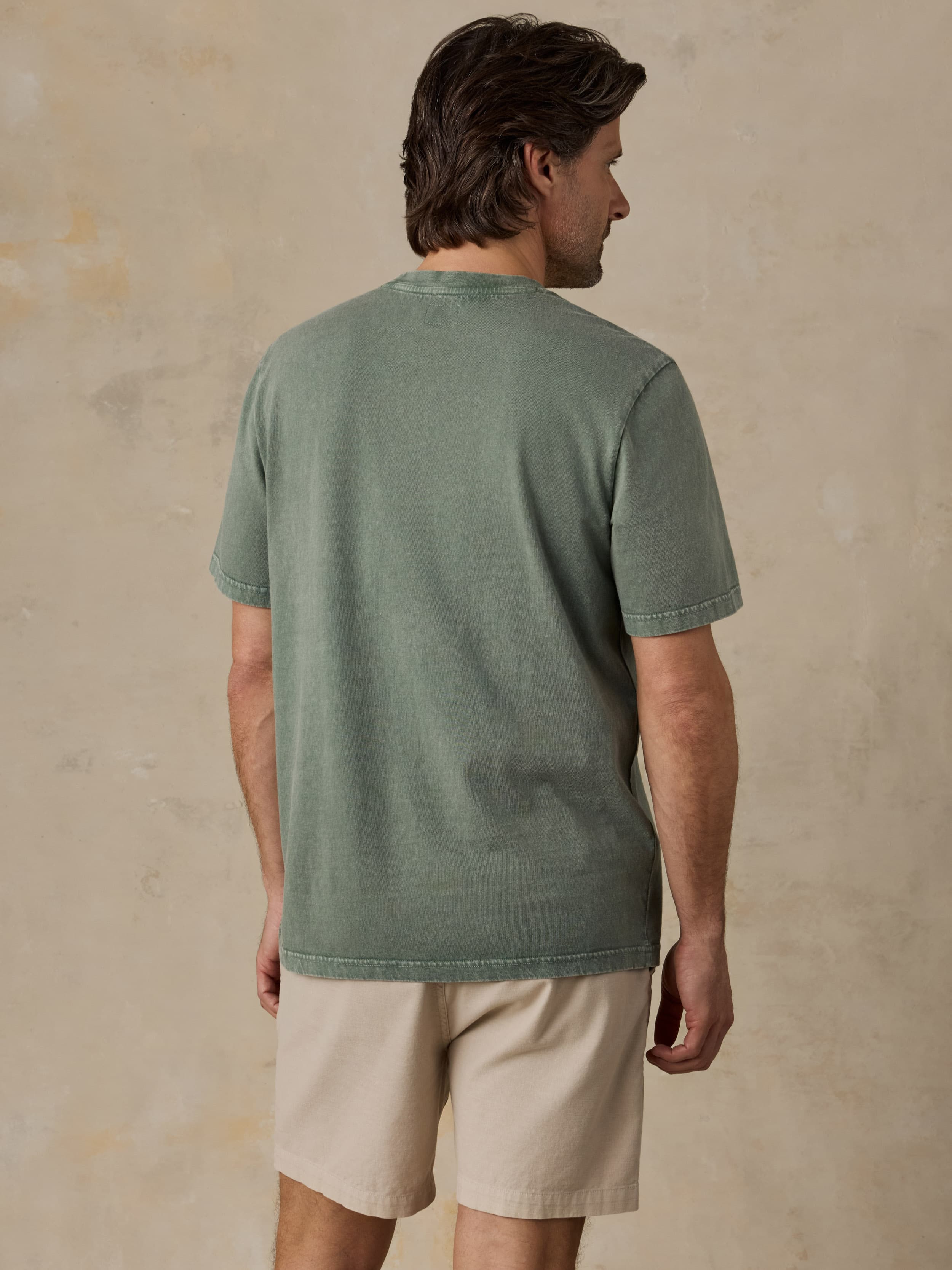 Man wearing a green t-shirt and beige shorts against a beige background