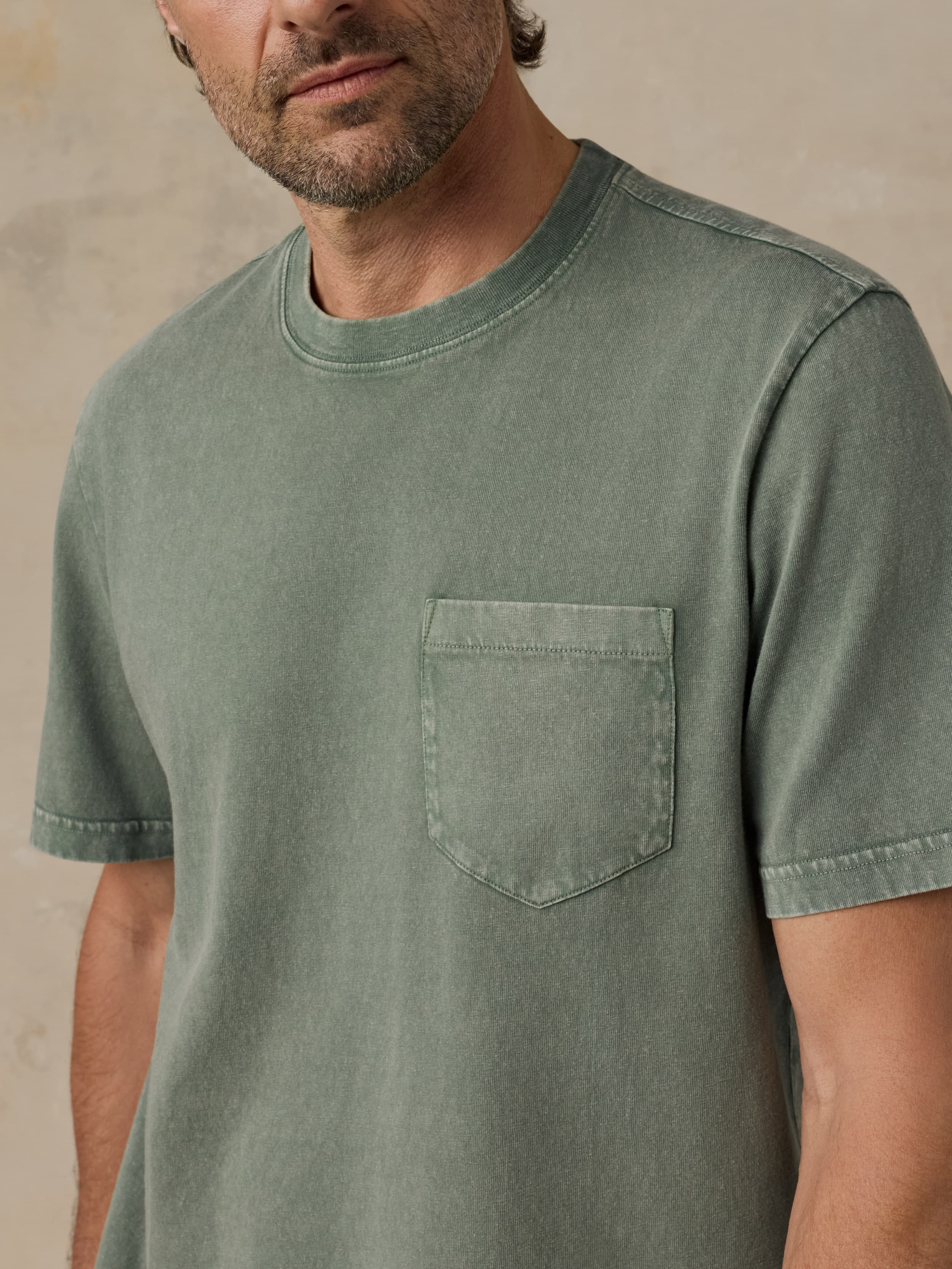 Man wearing a green t-shirt with a pocket against a beige background