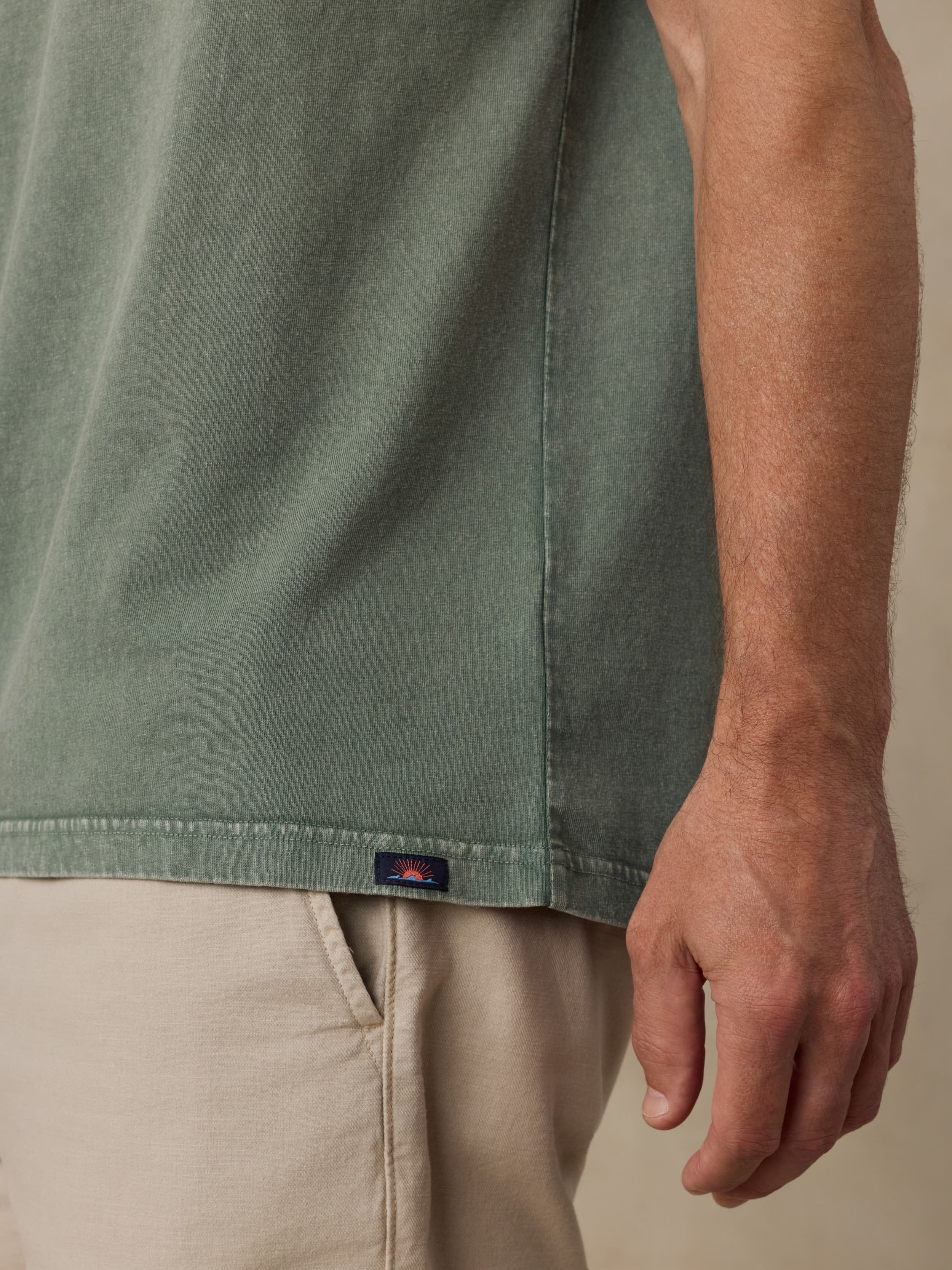Man wearing a green shirt with a Faherty brand logo and beige pants on a neutral background