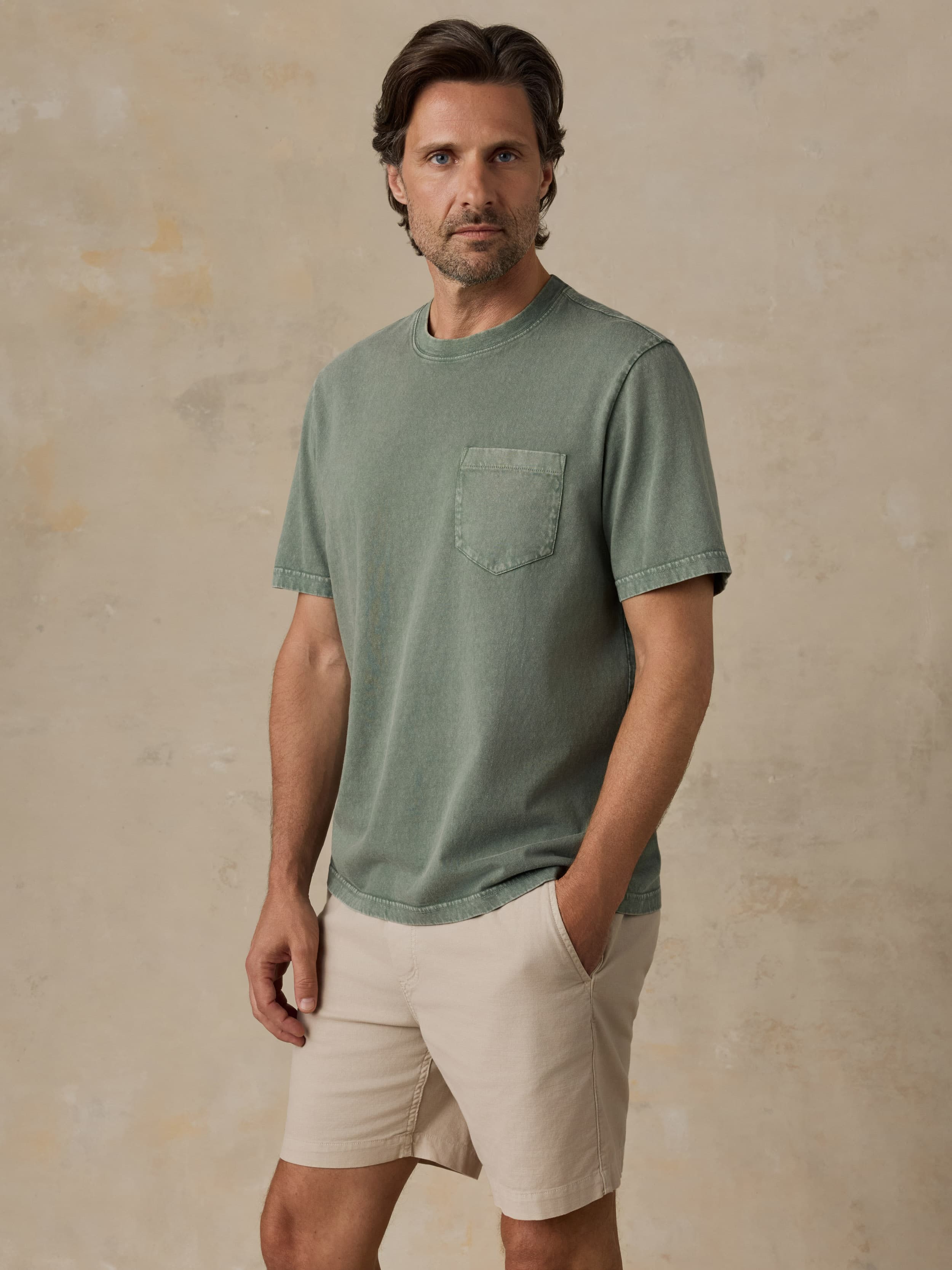 Man wearing a green t-shirt and beige shorts against a beige background