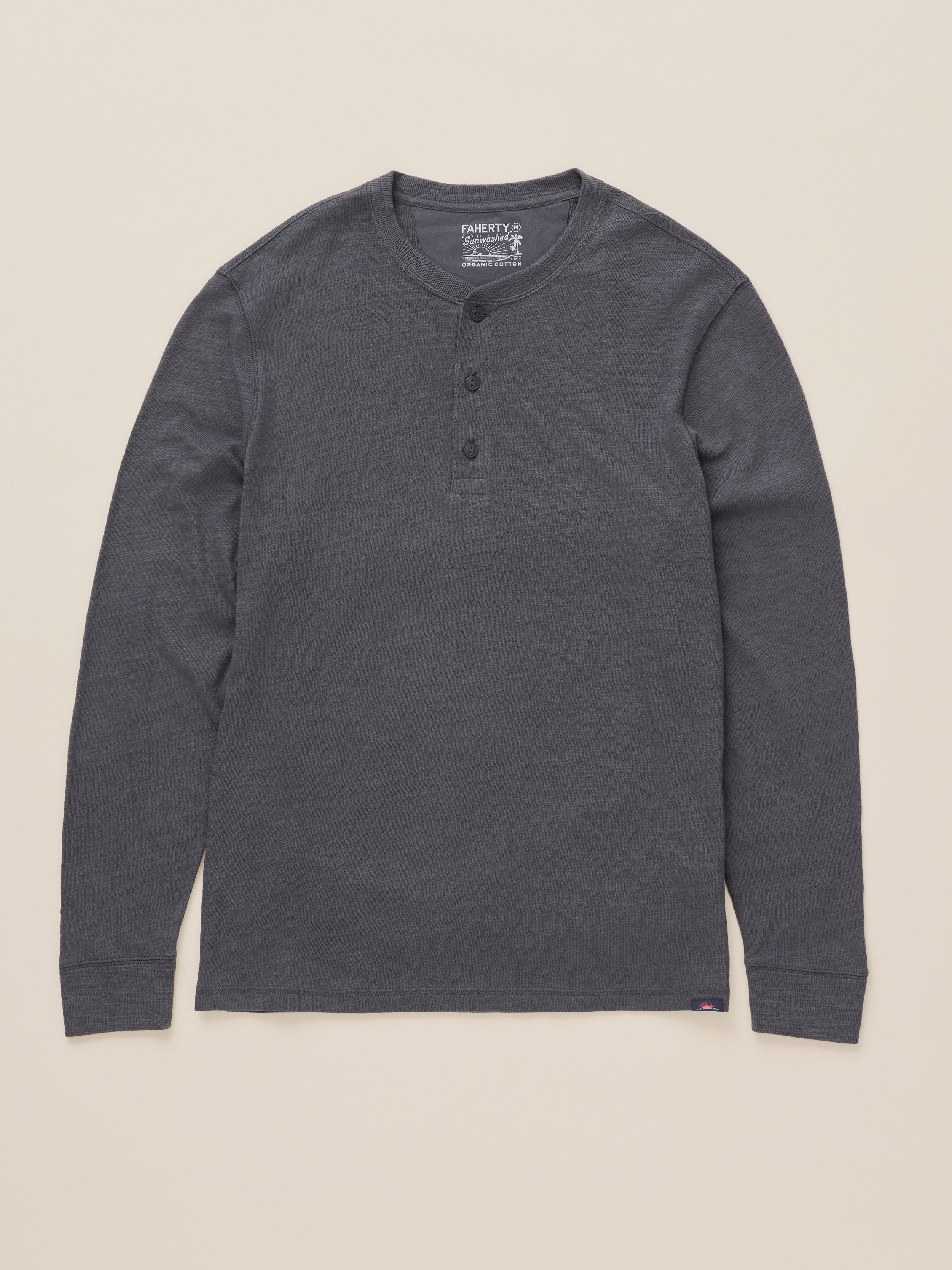 A dark gray long-sleeve henley shirt with three buttons on the chest, laid flat against a light beige background. The brand name Faherty is visible on the inner neck label.