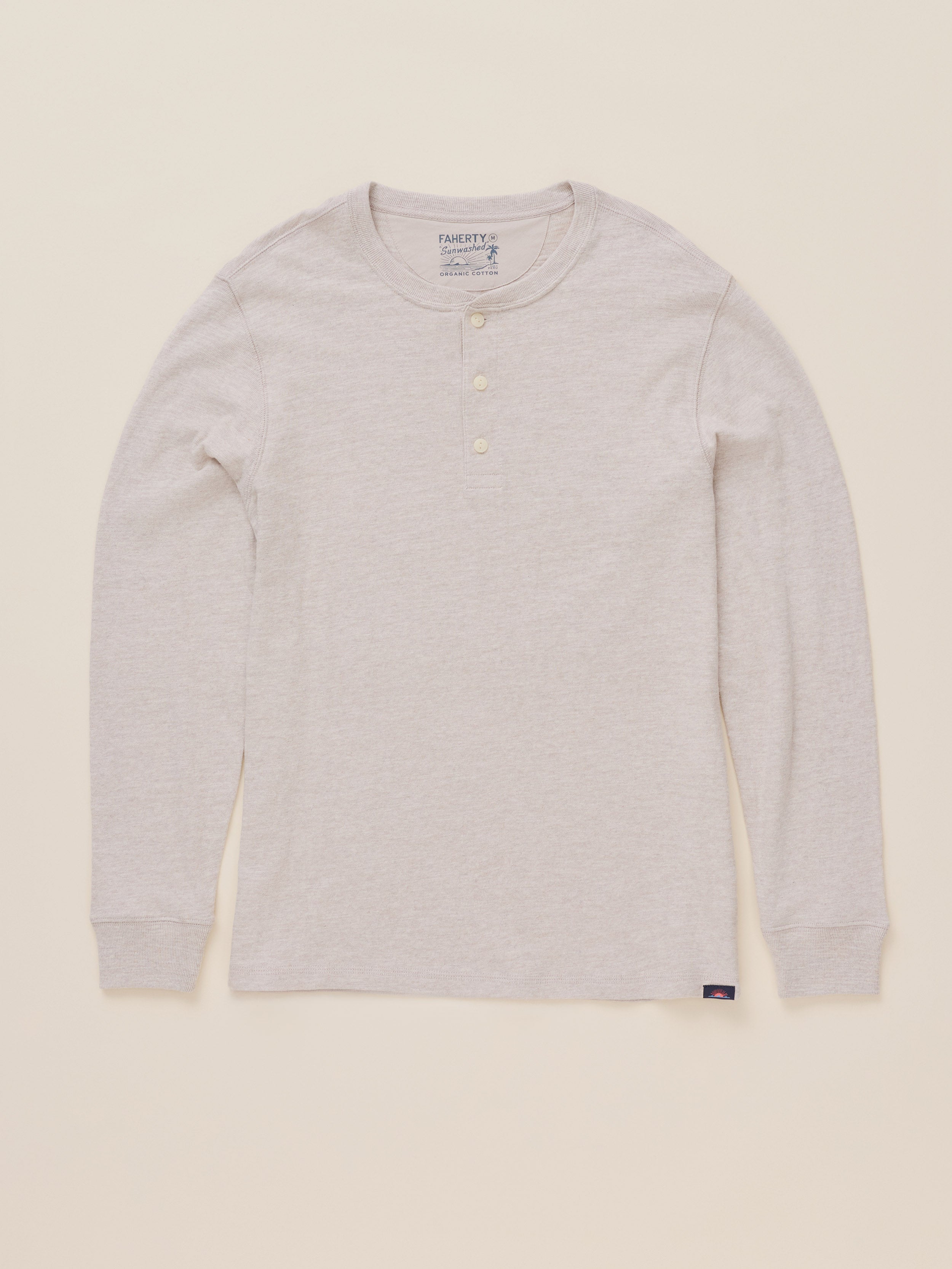 A light oatmeal heather long-sleeve henley shirt with three buttons on the collar, laid flat against a warm cream background.