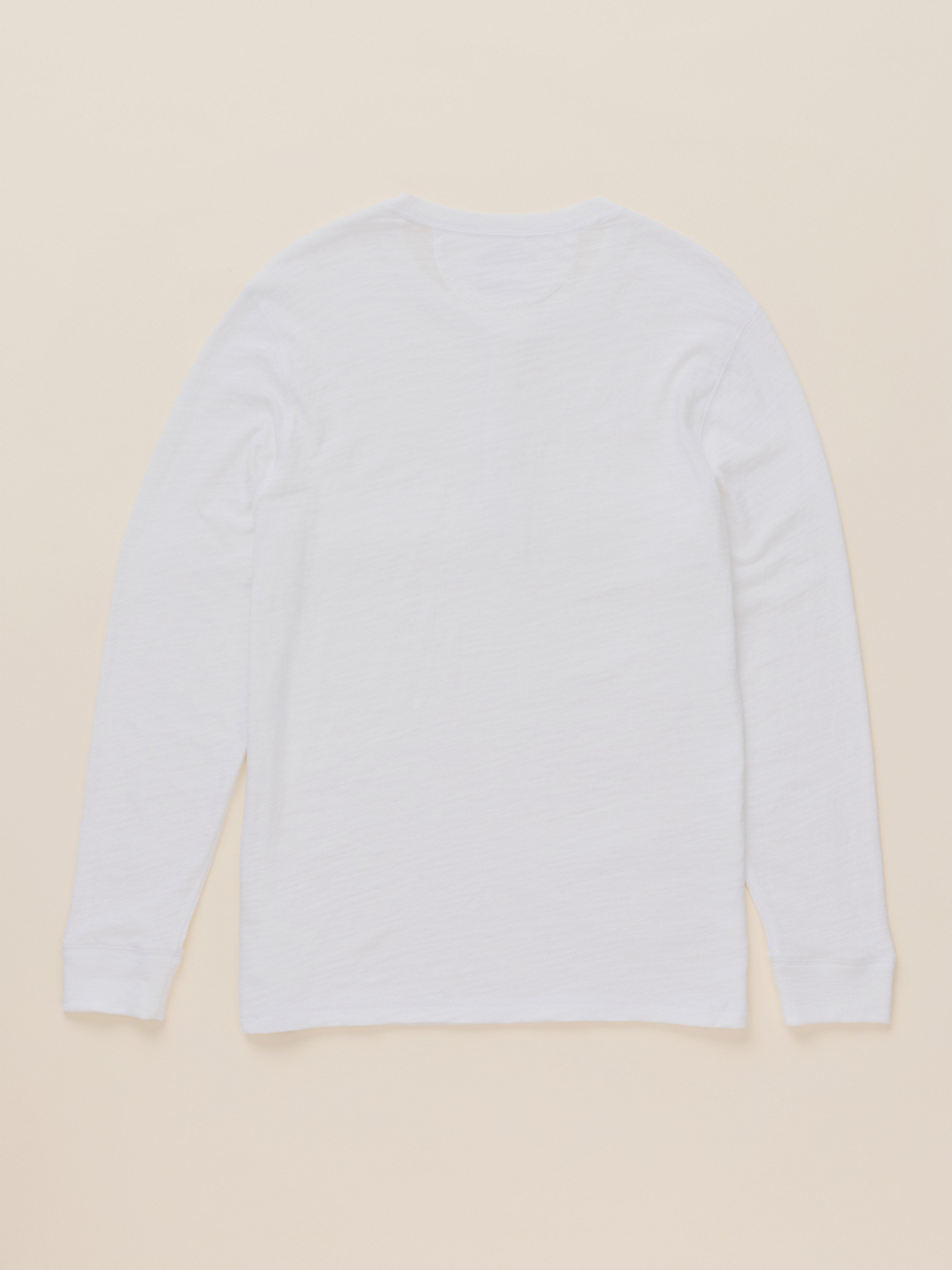 A plain white long-sleeve crewneck shirt laid flat against a light beige background.